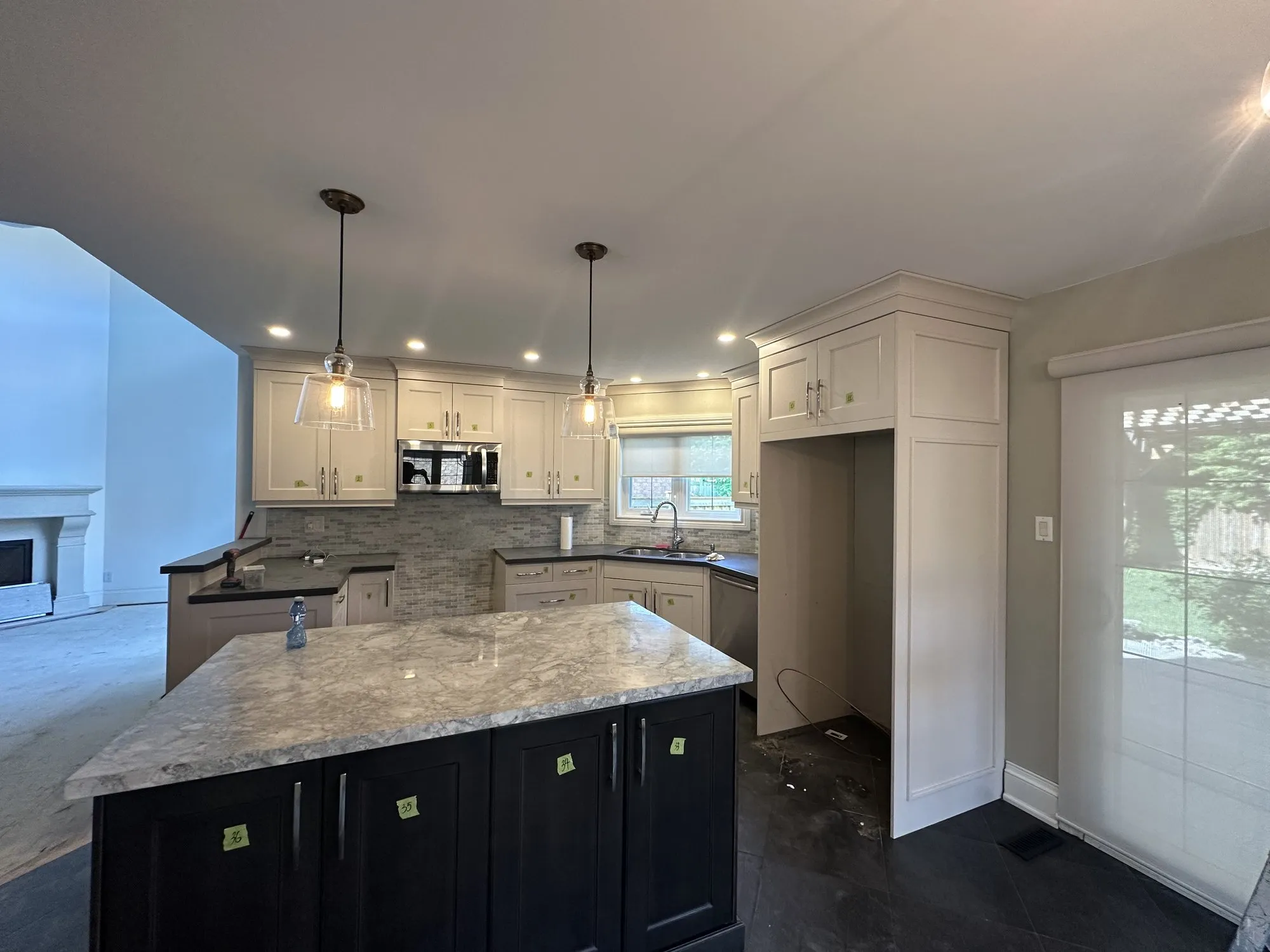 The kitchen before the work with numbered tape on every door, the perimeter cabinets a warm cream and the island dark brown