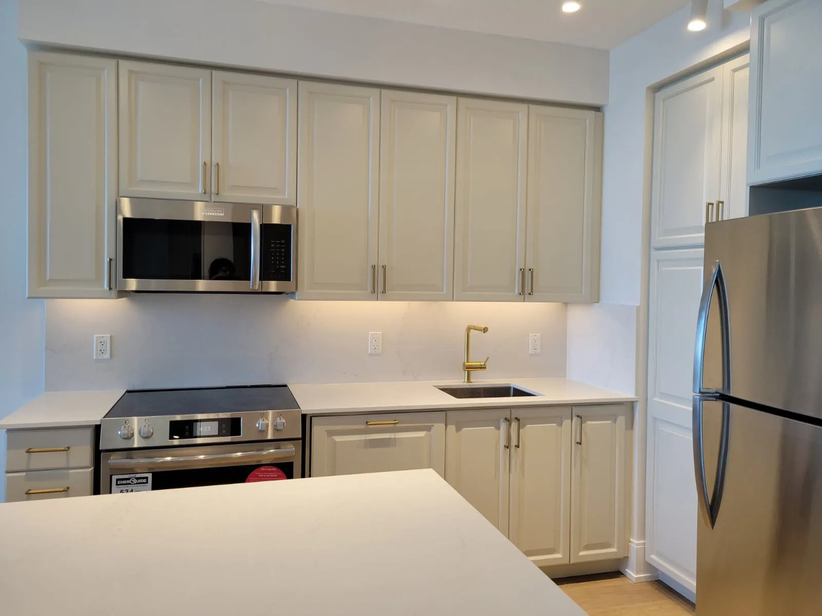 The finished range wall — cream raised-panel doors with brass bar handles, a stainless range and microwave, and a quartz counter running into a slab backsplash