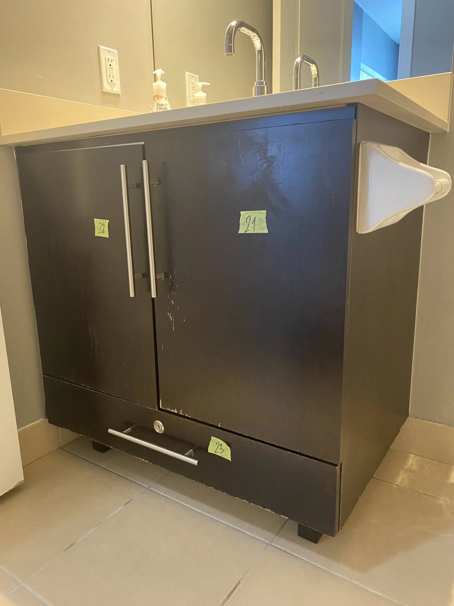 The bathroom vanity before any work, in dark espresso, its doors numbered with tags ready to come off