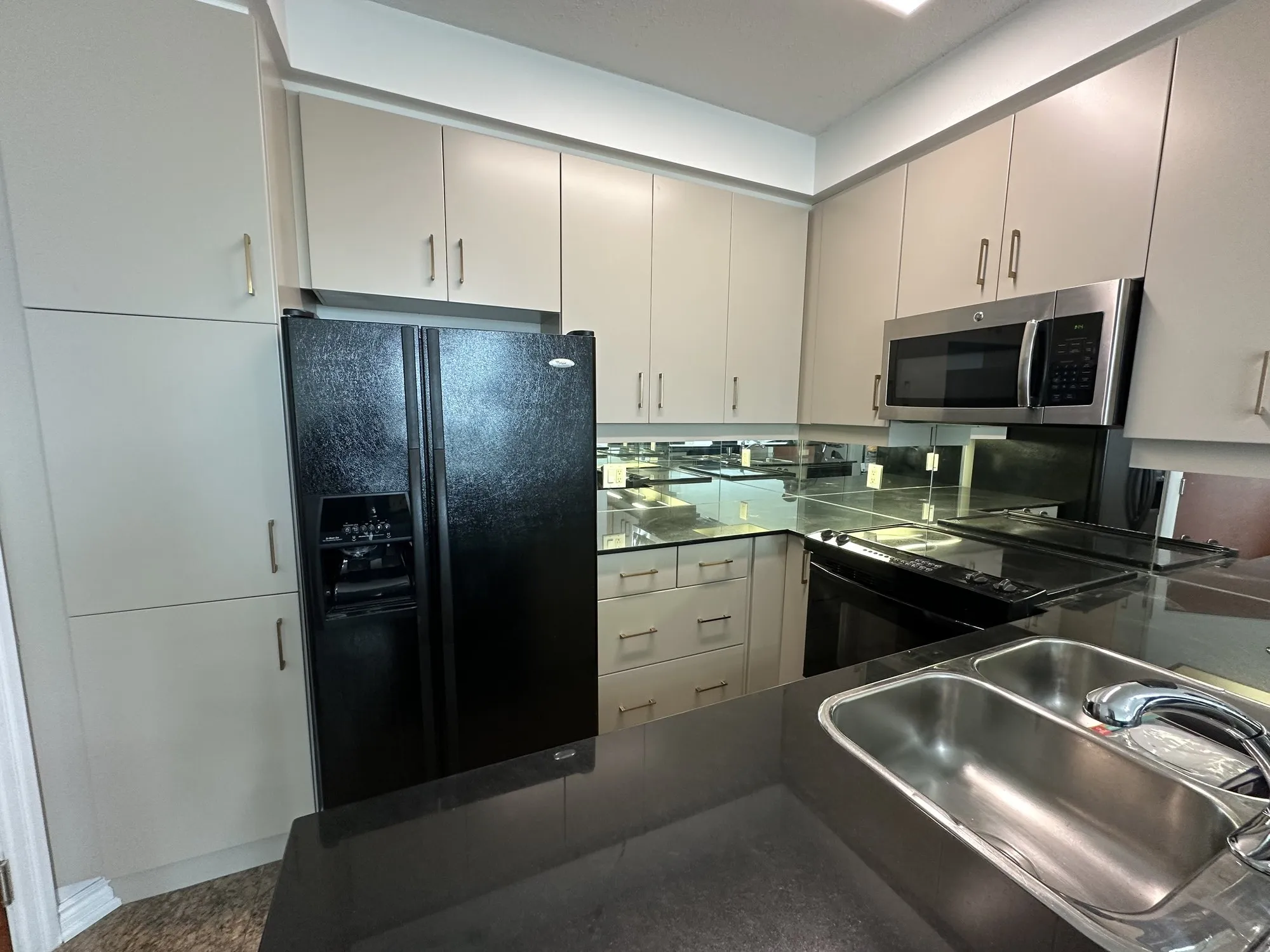 The finished galley run, cabinets sprayed a warm off-white with brass bar pulls, the black granite and mirrored backsplash unchanged
