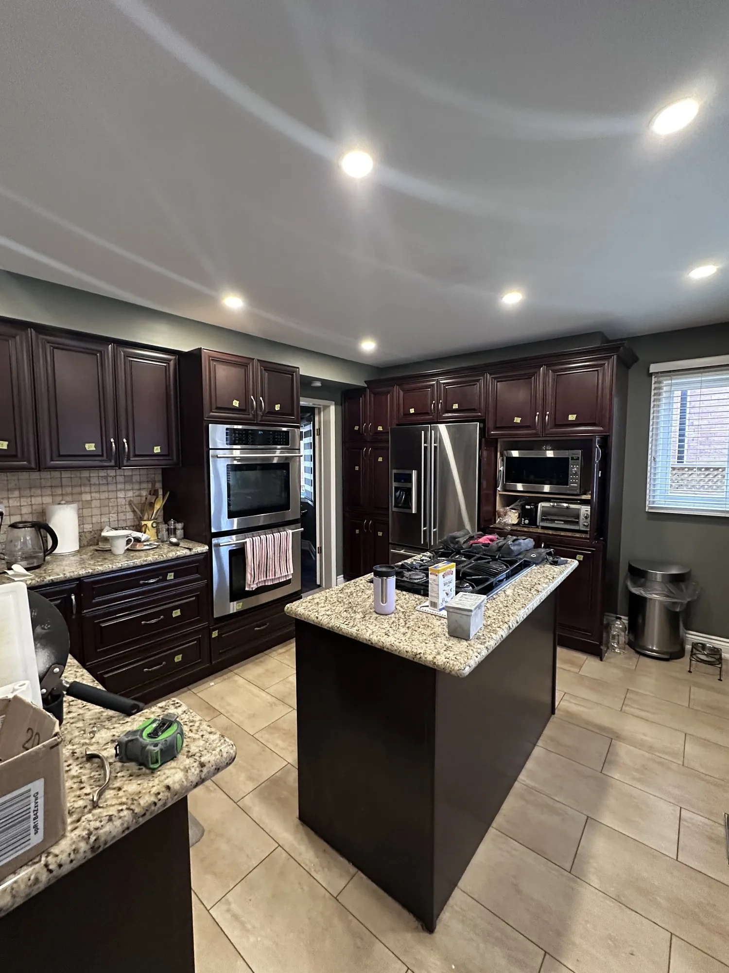 The kitchen before the work, espresso cabinetry around an island with speckled granite counters and a tiled floor
