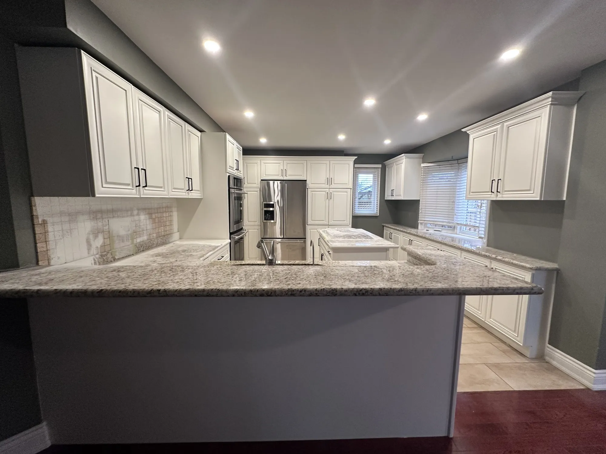 The finished kitchen in a warm cream with the same granite counters, peninsula and island, and the tile and hardwood floors unchanged