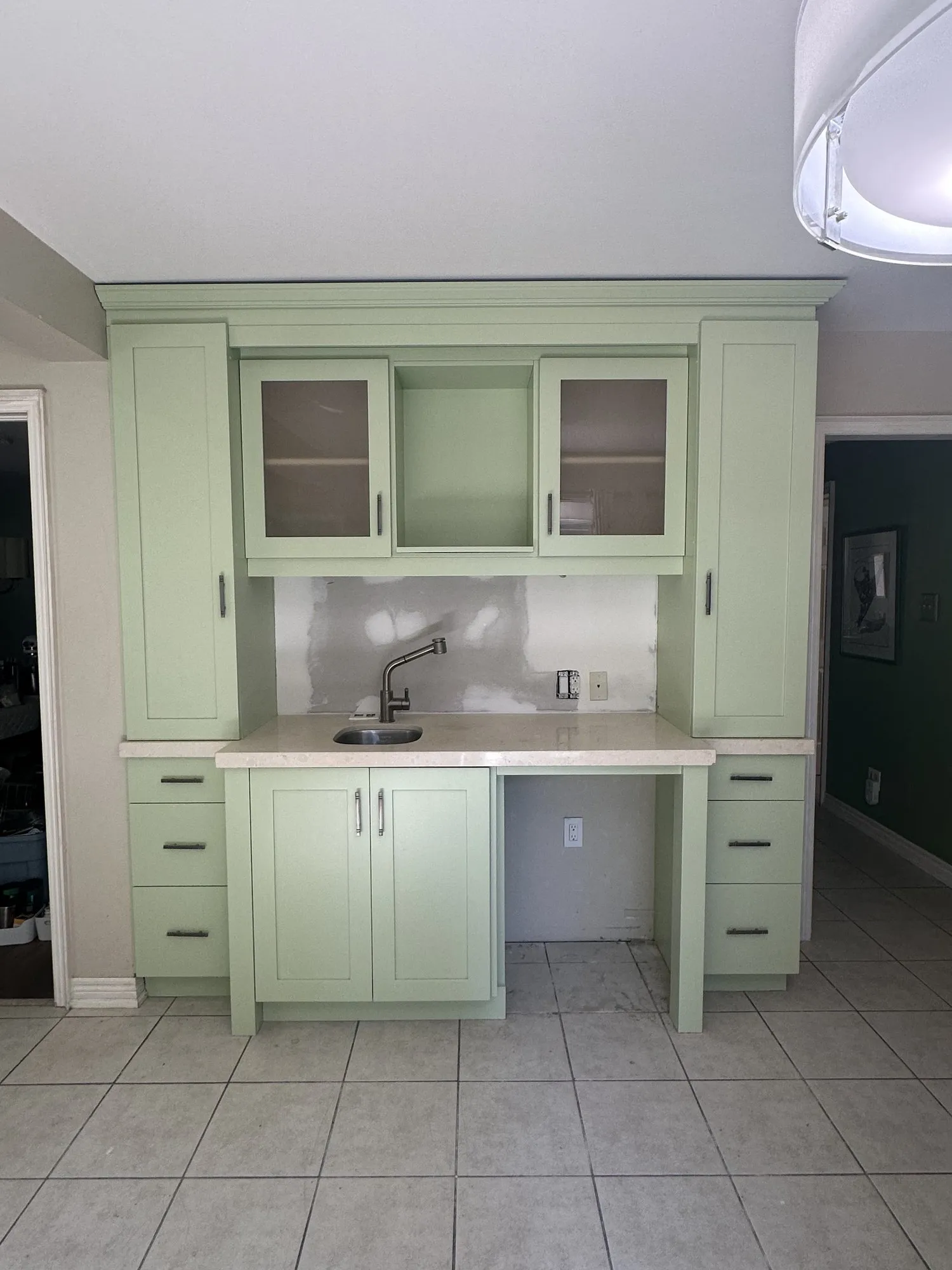 The built-in desk and beverage unit at the end of the kitchen, sprayed the same light green, with glass-fronted uppers, a small bar sink and drawers either side of the knee-hole