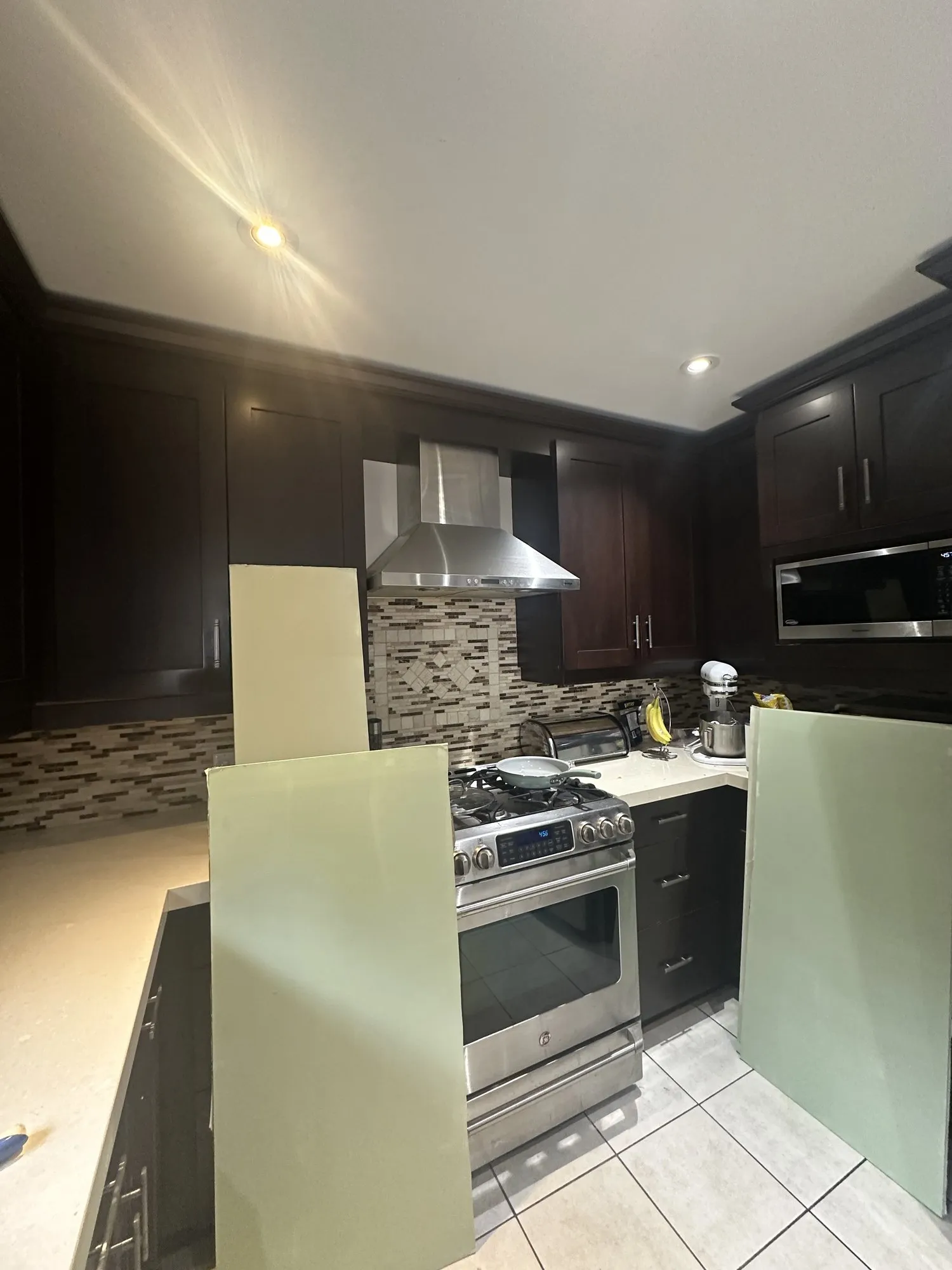 Two side panels sprayed light green standing on the floor in front of the range, with the rest of the kitchen still espresso