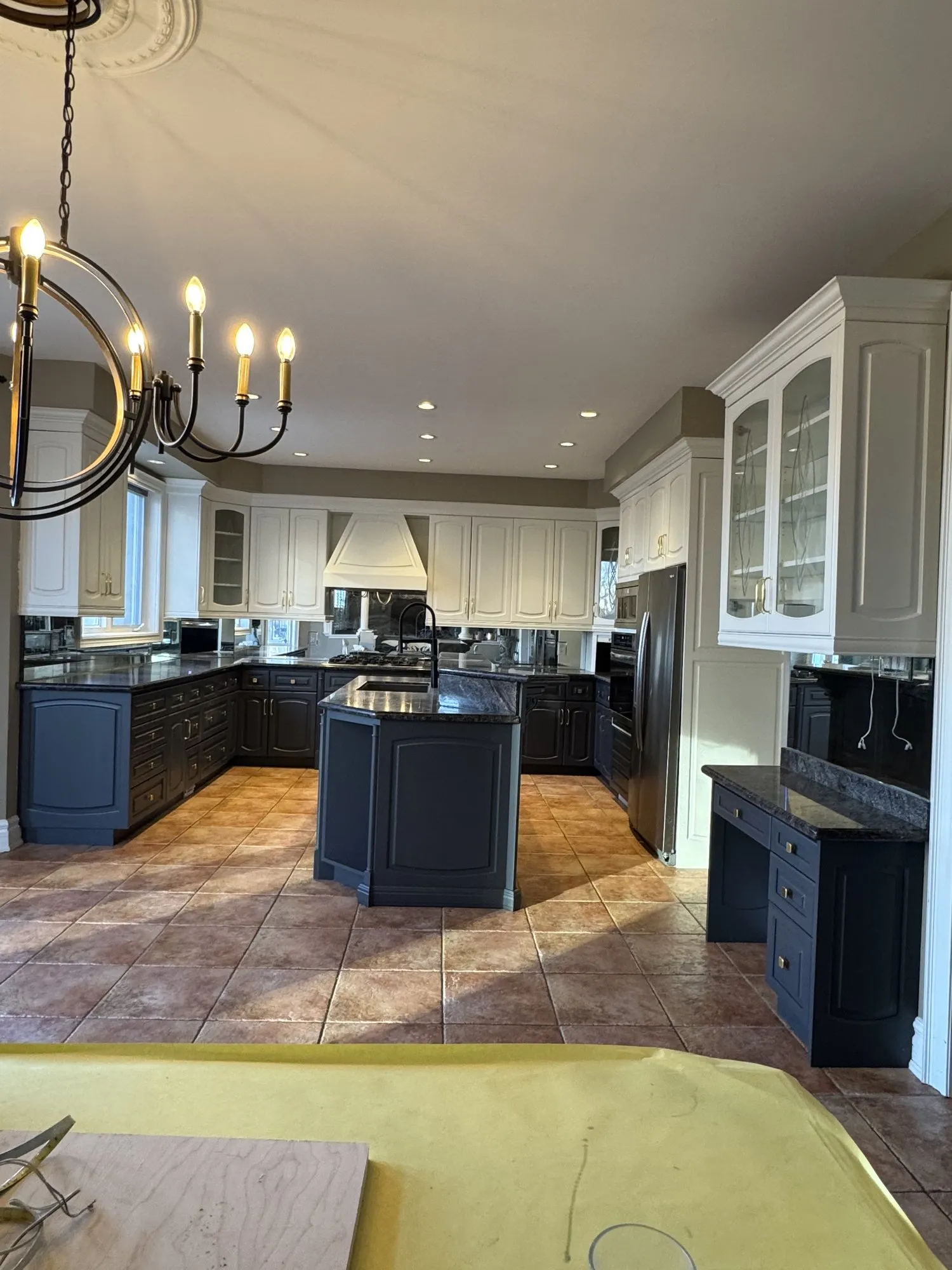 The finished kitchen with white upper cabinetry, a navy island and navy lower cabinets, and the original granite and floor kept
