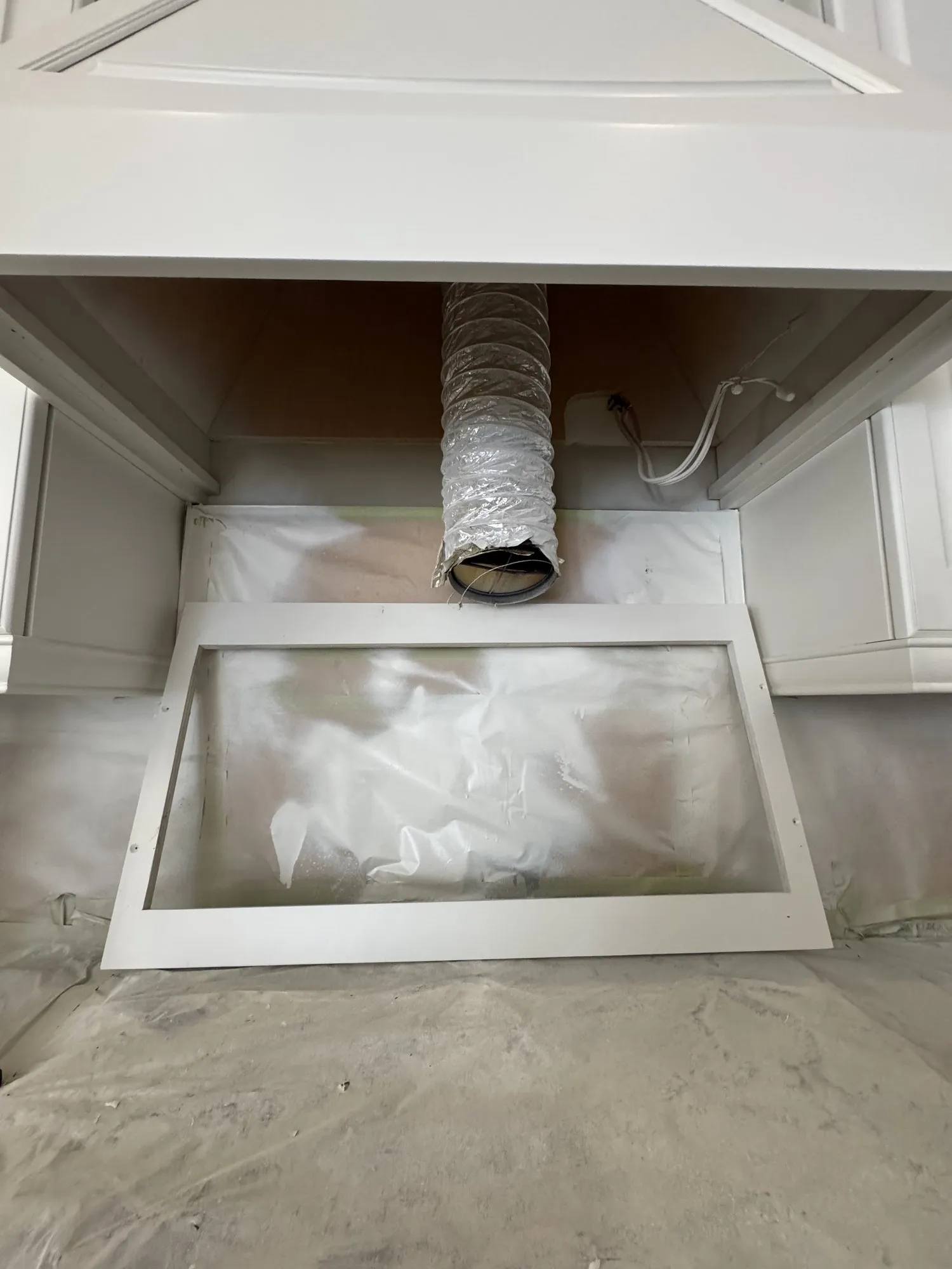 The range opening with the old hood removed and ducting exposed, and a new white hood insert base standing ready on the floor