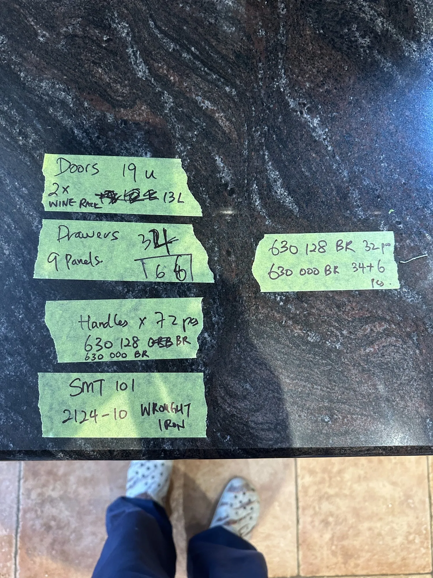 Handwritten notes on green tape stuck to the granite counter, listing door, drawer, panel and handle counts with hardware codes