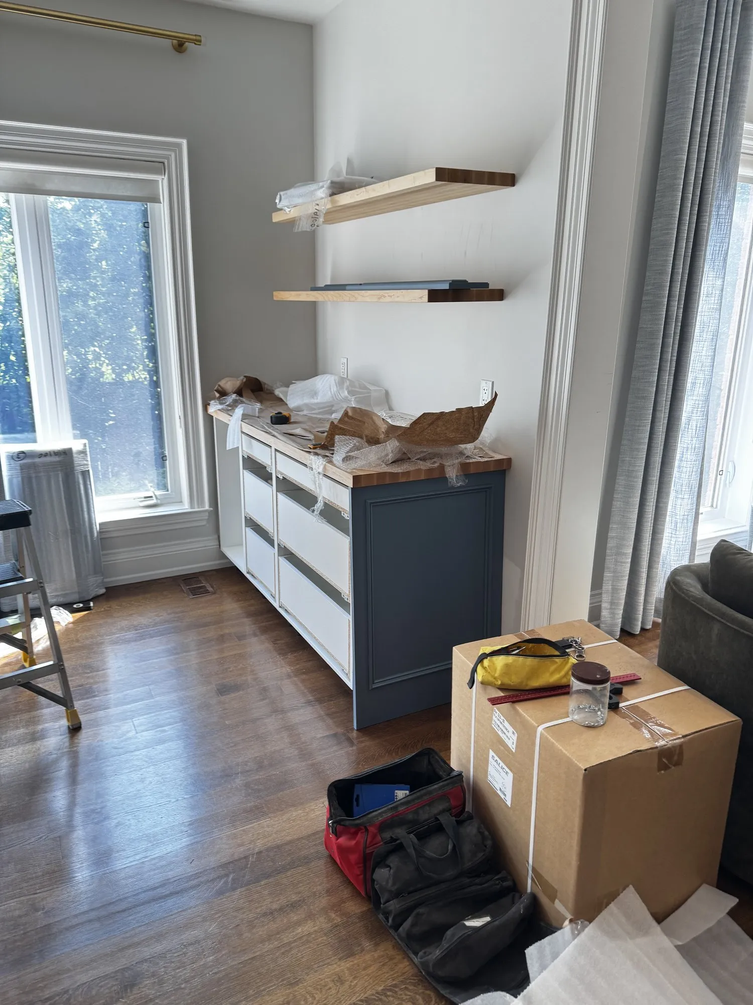 The new coffee station part-built against a bare wall, the blue carcase and butcher-block top in place with two floating shelves already mounted above and the drawer boxes still unfronted