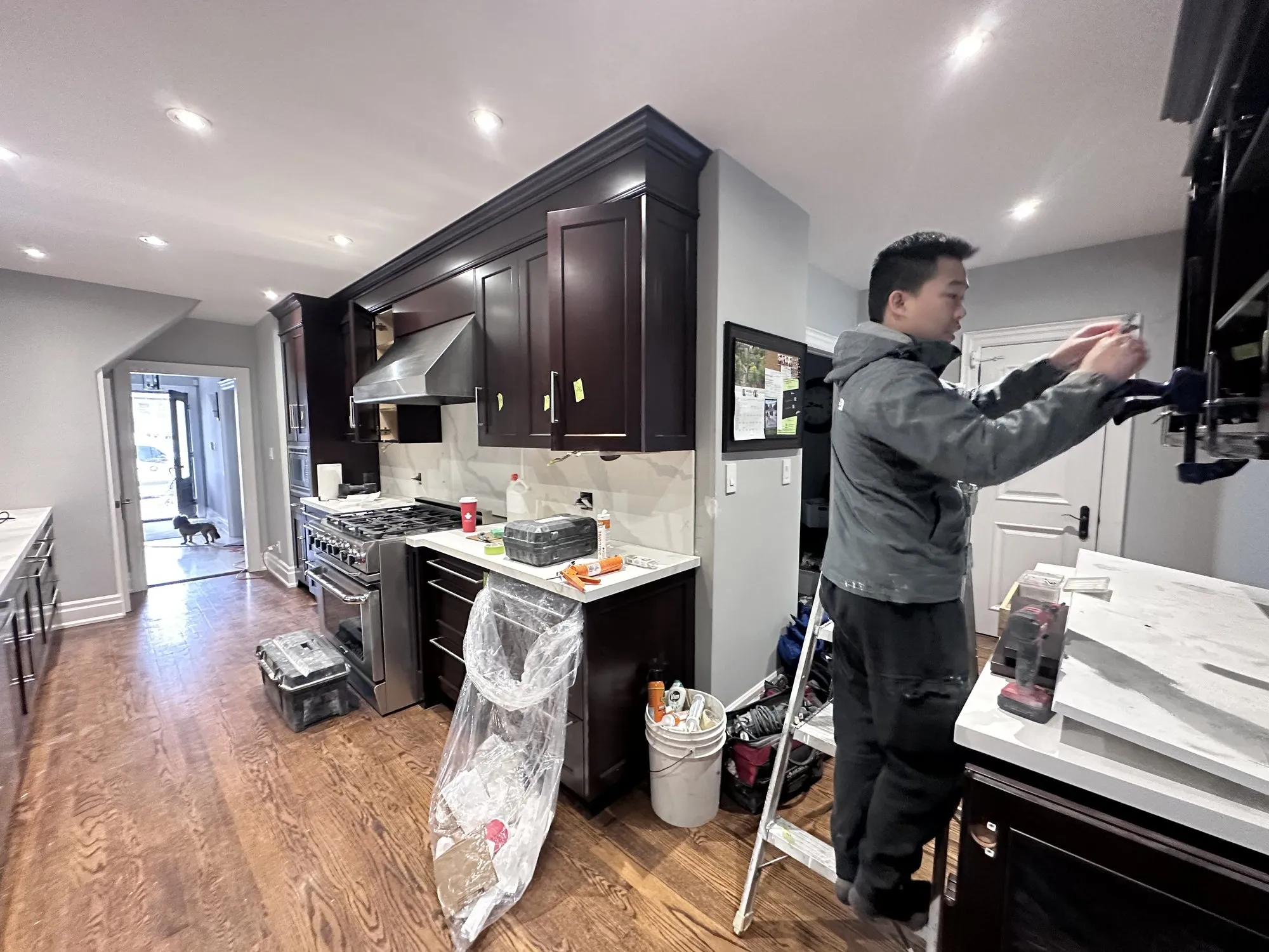 The kitchen sealed in plastic and tape with the frames masked, and a sprayer working from a stepladder inside the containment