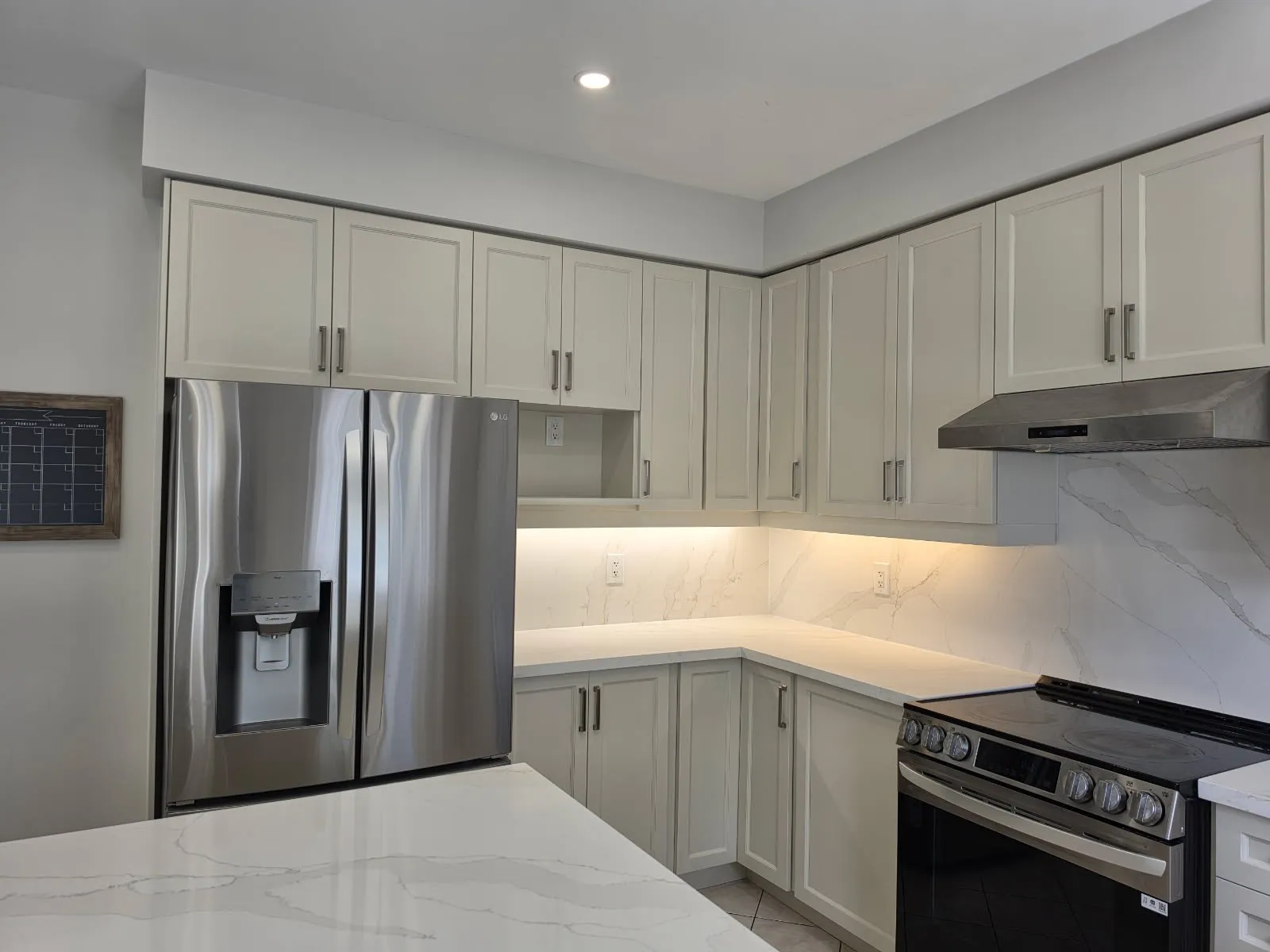 The finished kitchen with cream cabinetry, new white quartz counters and a full-height slab backsplash behind the range