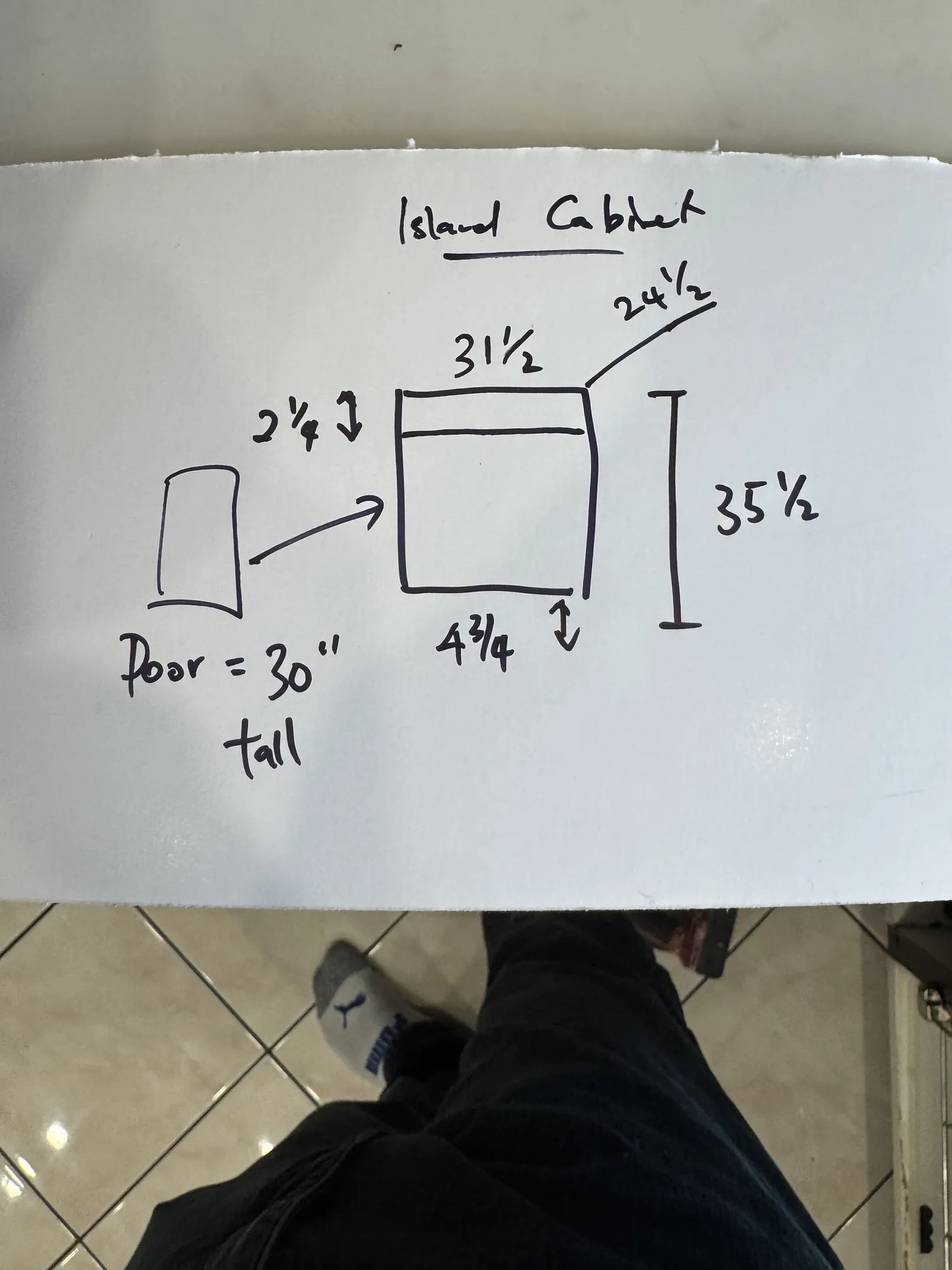 A hand-drawn sketch of the new island cabinet with its width, depth and height dimensions written on it, photographed on the kitchen floor