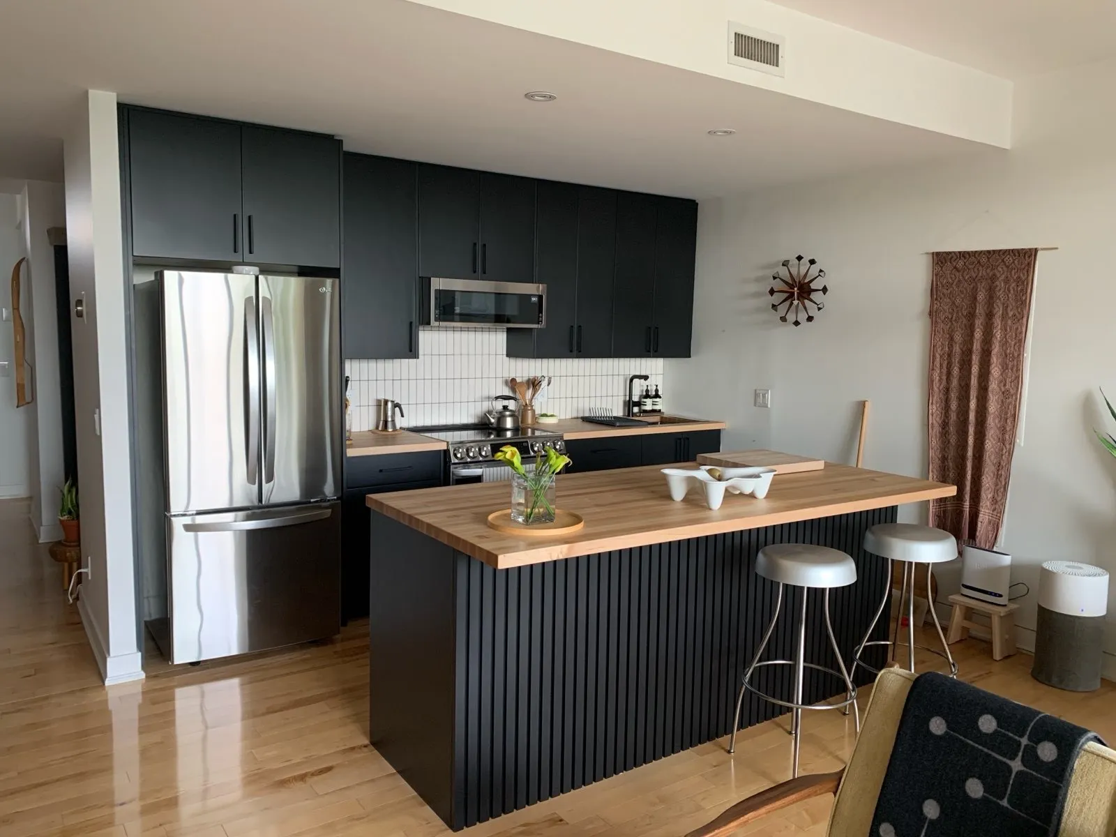 The finished island with a black slatted front and a butcher-block top, the surrounding cabinetry sprayed the same near-black