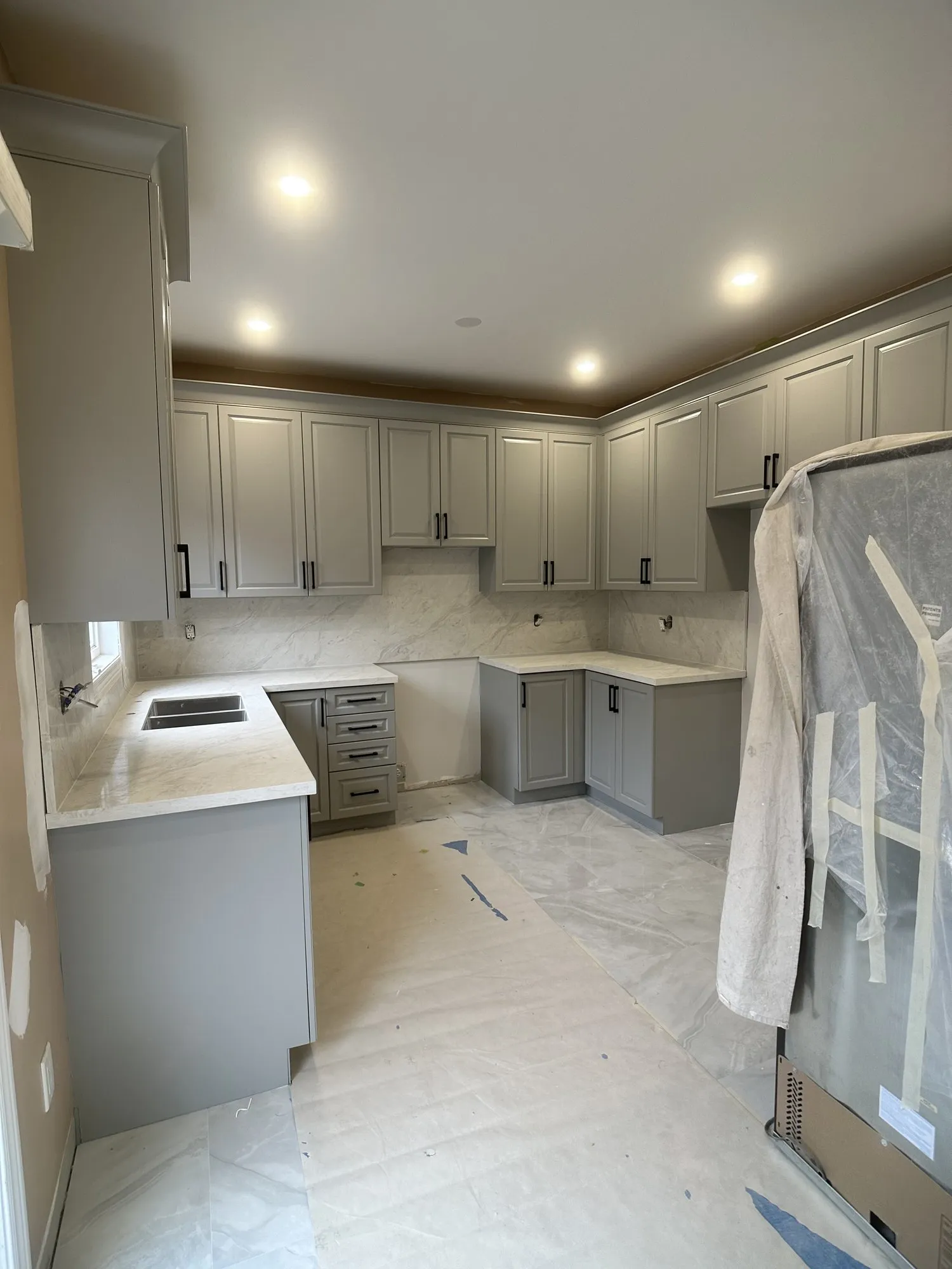 The kitchen sprayed Platinum Gray with the doors rehung, floors still fully covered and the appliances not yet moved back in