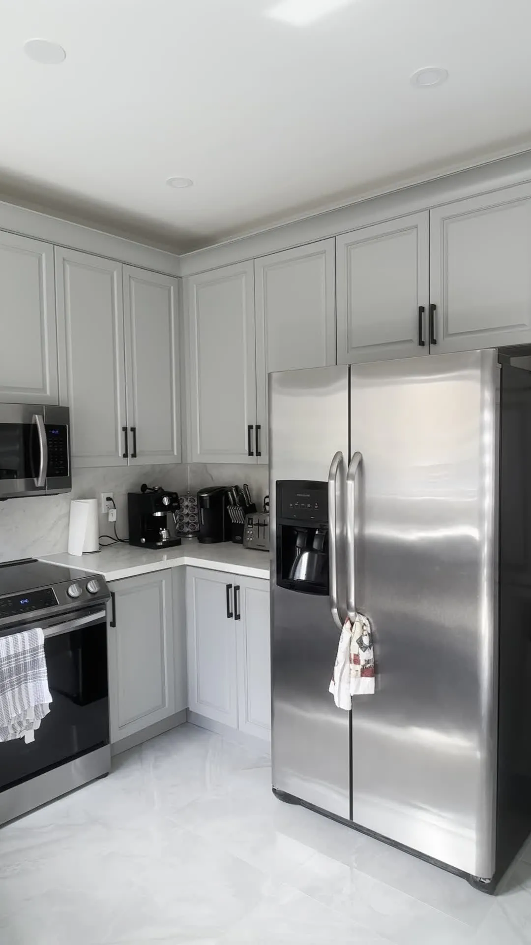 The finished Vellore Village kitchen — Platinum Gray cabinetry with matte black bar pulls, crown moulding running the top of the uppers, and the original quartz and marble backsplash kept
