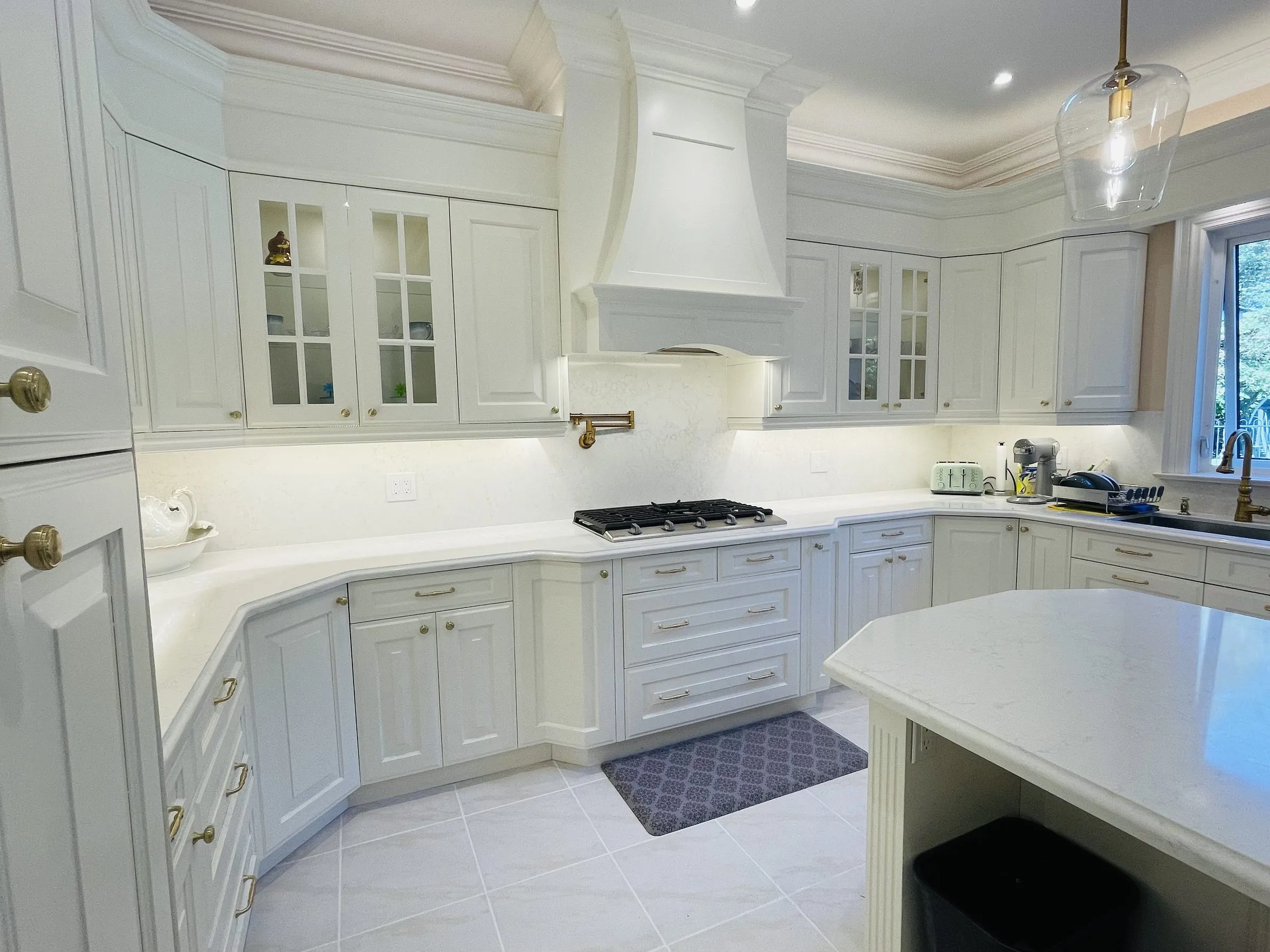 A kitchen refaced by Kitchen Made New in Gormley — white raised-panel doors, a custom range hood and quartz worktops running to the island