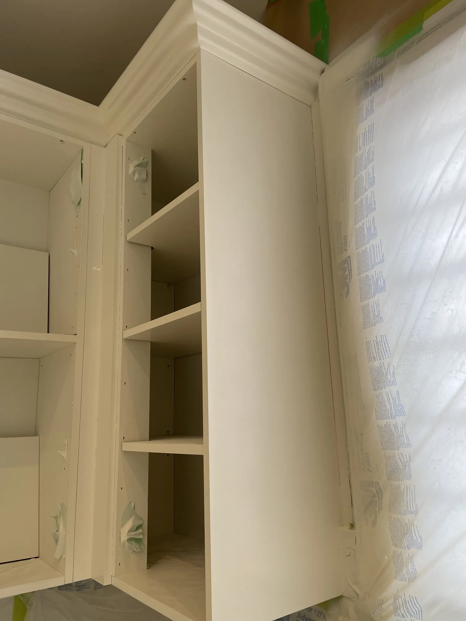 An open corner shelving unit part way through, its frame sprayed white while the containment sheeting still hangs beside it