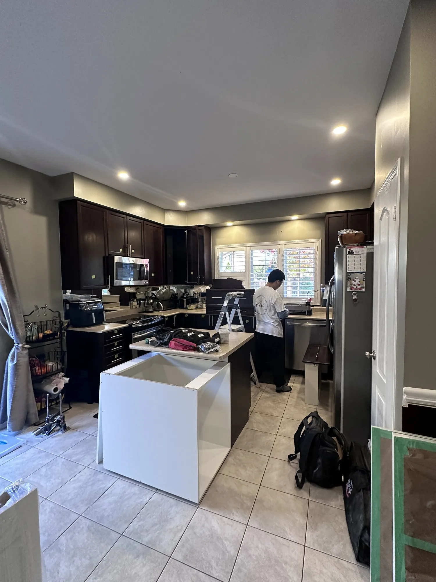 A new white cabinet box standing against the end of the existing dark espresso island, part way through installation, with the rest of the kitchen still dark
