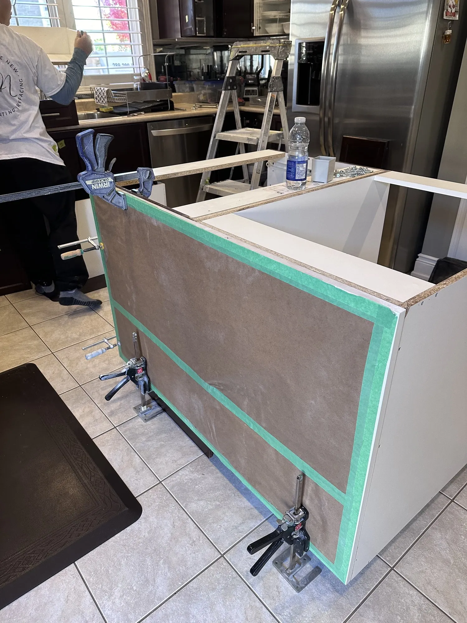 The island end panel clamped and taped in place while the adhesive sets, the new white carcass visible behind it