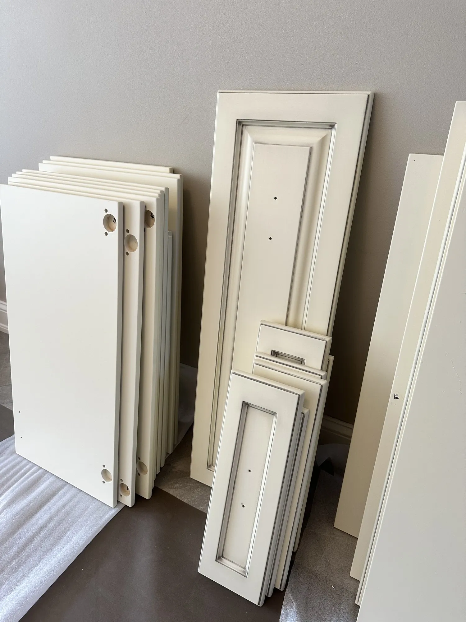 New doors and panels stacked against a wall, already finished cream and glazed to match the existing kitchen
