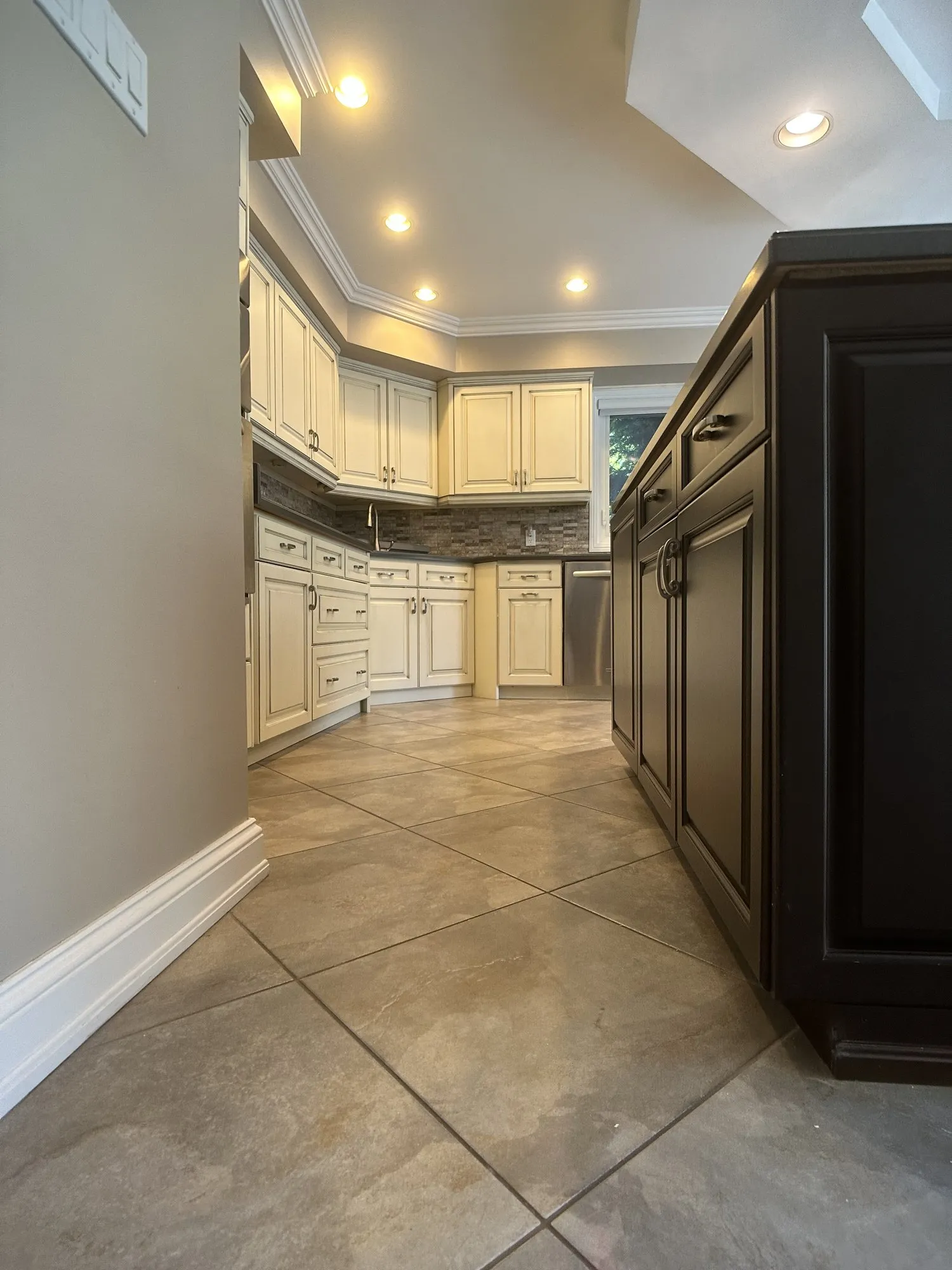The finished run of cream glazed cabinetry beside the dark island, with the new under-sink cabinetry sitting in it unnoticed