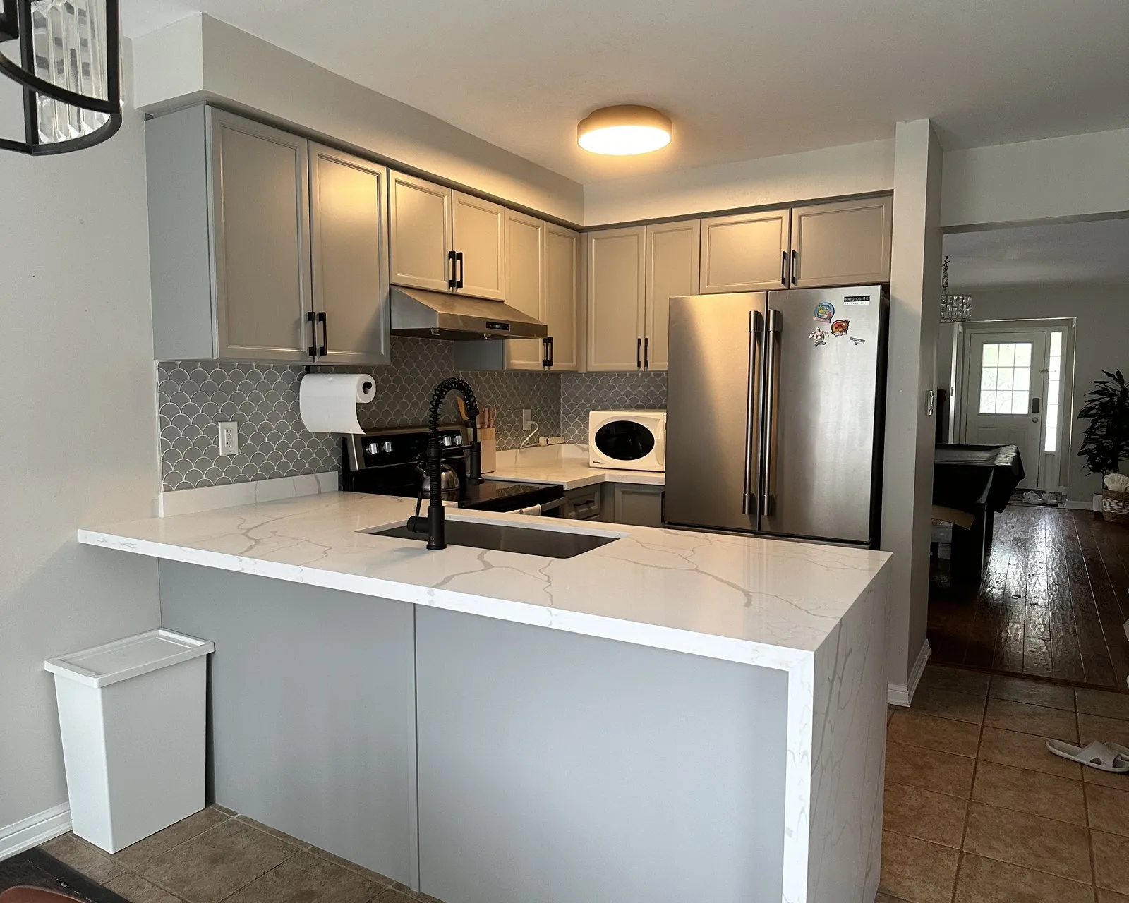 After — The same kitchen before and after a countertop replacement — laminate tops swapped for white quartz with a waterfall end, the painted cabinets untouched