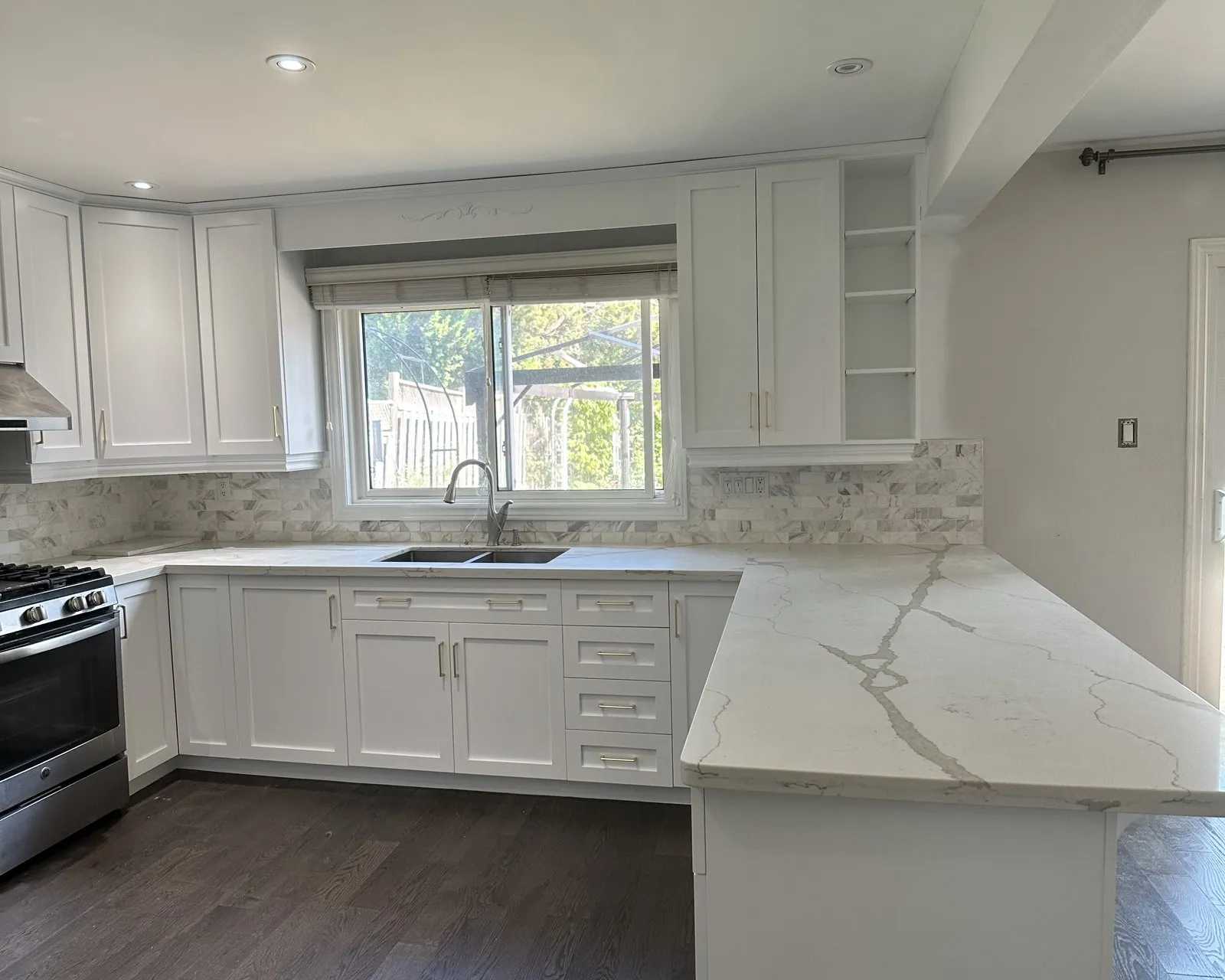 After — A kitchen before and after — oak fronts replaced with white and new veined stone run across the counters, the range wall and window unchanged