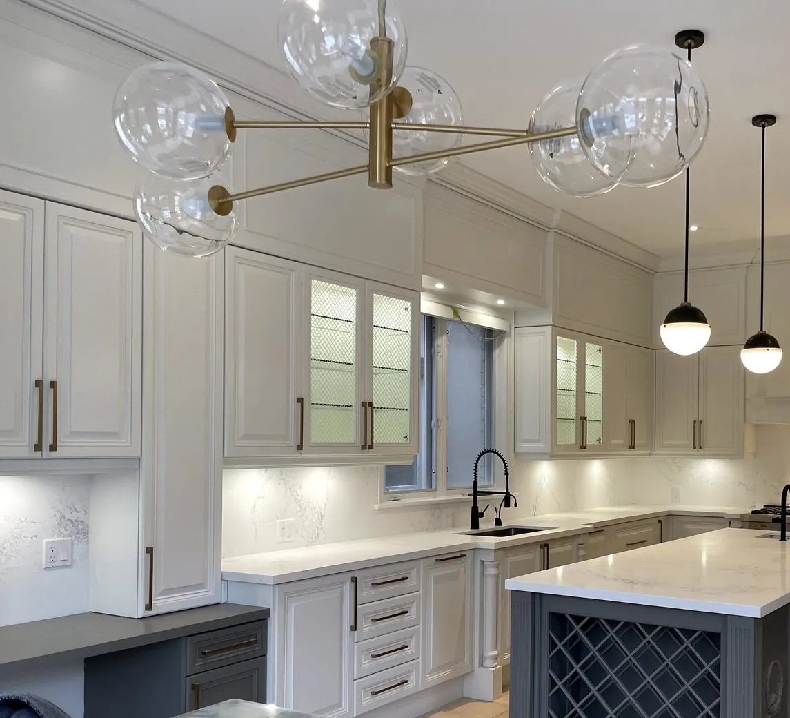 After — A kitchen before and after — antiqued cream raised-panel cabinets with a glazed finish replaced by white, the island refinished charcoal and keeping the lattice wine rack it already had