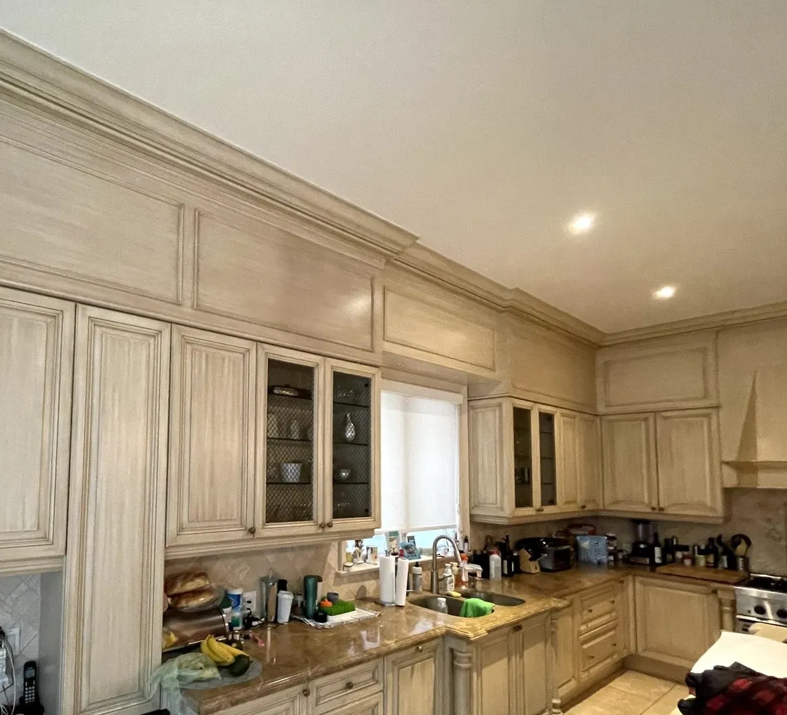 Before — A kitchen before and after — antiqued cream raised-panel cabinets with a glazed finish replaced by white, the island refinished charcoal and keeping the lattice wine rack it already had