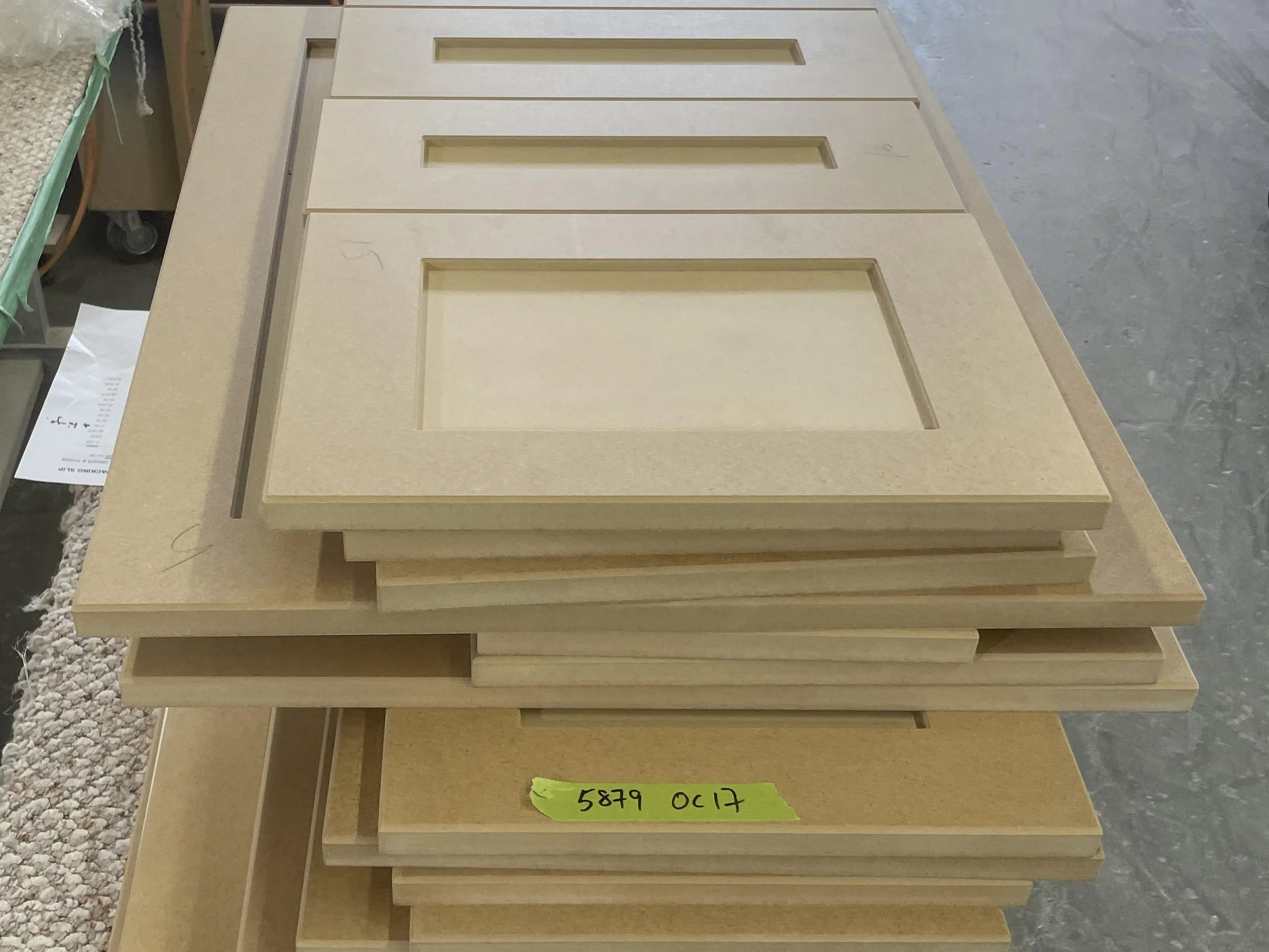 New shaker doors stacked on a padded trolley in the shop before finishing, the machined panel and the door edges visible down the stack