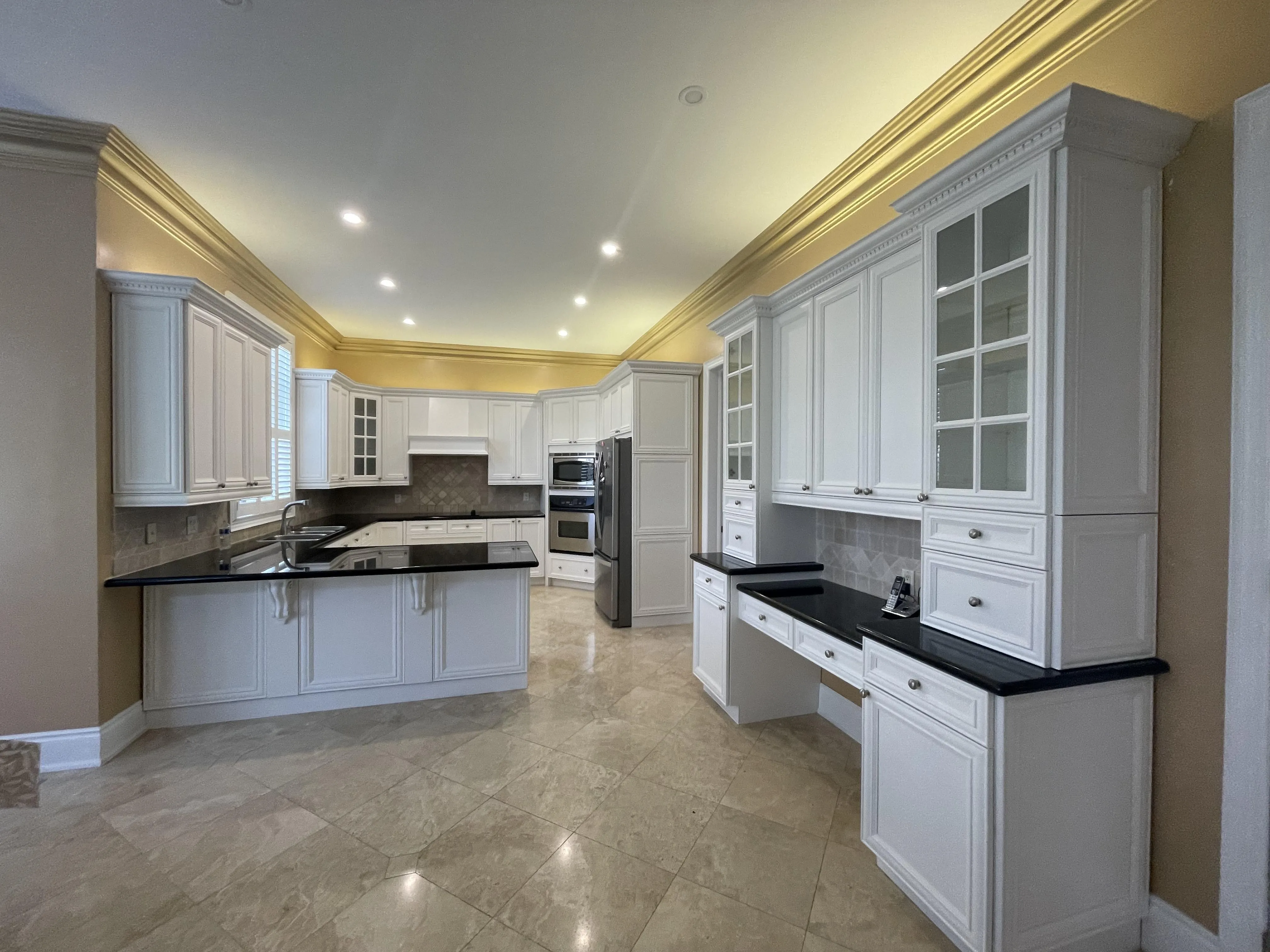 A large white kitchen — a peninsula, a full wall of uppers, a built-in desk run and glass-front cabinets, with dozens of doors and drawer fronts in the one room