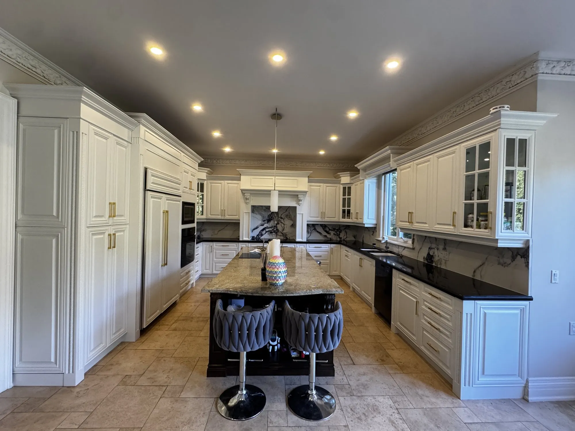 A finished kitchen: white raised-panel cabinets with gold bar pulls, black countertops, a granite island and a stone floor