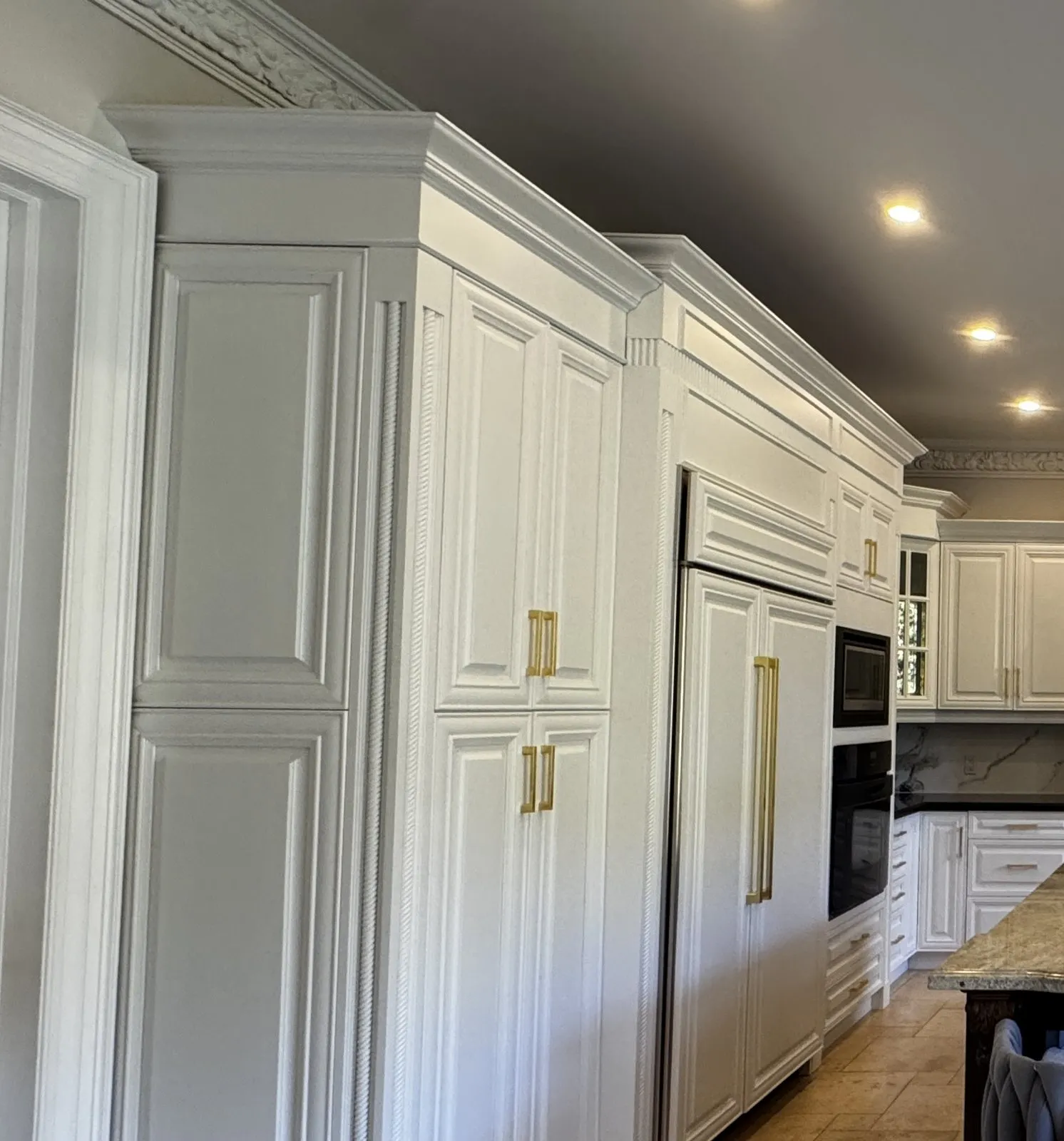 Tall white pantry cabinets and panelled fridge doors with gold pulls and a carved pilaster