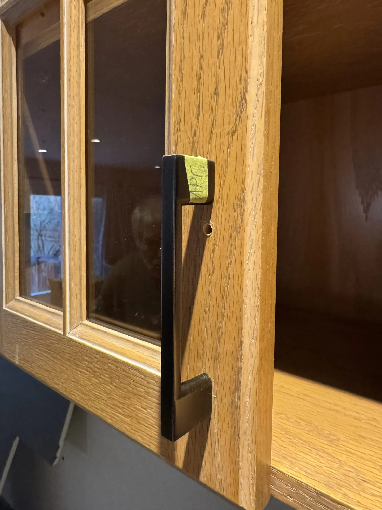 A new antique pewter bar pull held against one of the original golden oak glass-front doors before the kitchen was sprayed