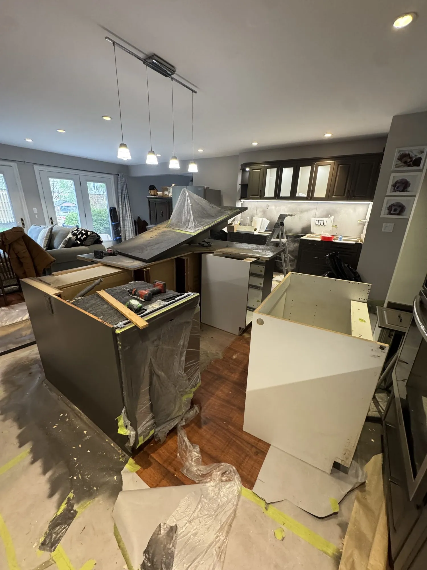 The sink run stripped out, the old countertop lifted off and two new white cabinet carcasses standing ready, with the floor papered and taped