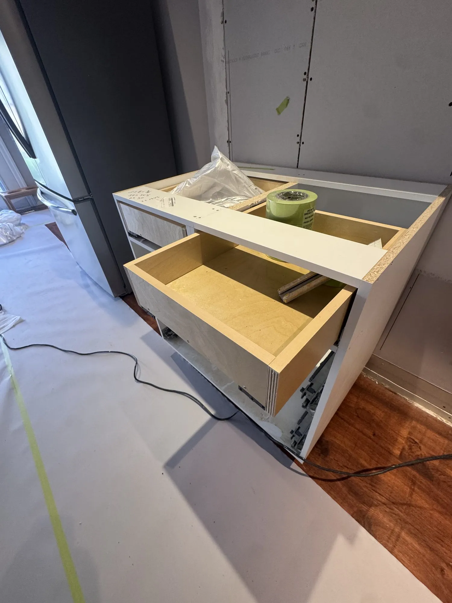 A plywood drawer box pulled open in one of the new cabinets, the natural ply visible against the white carcass