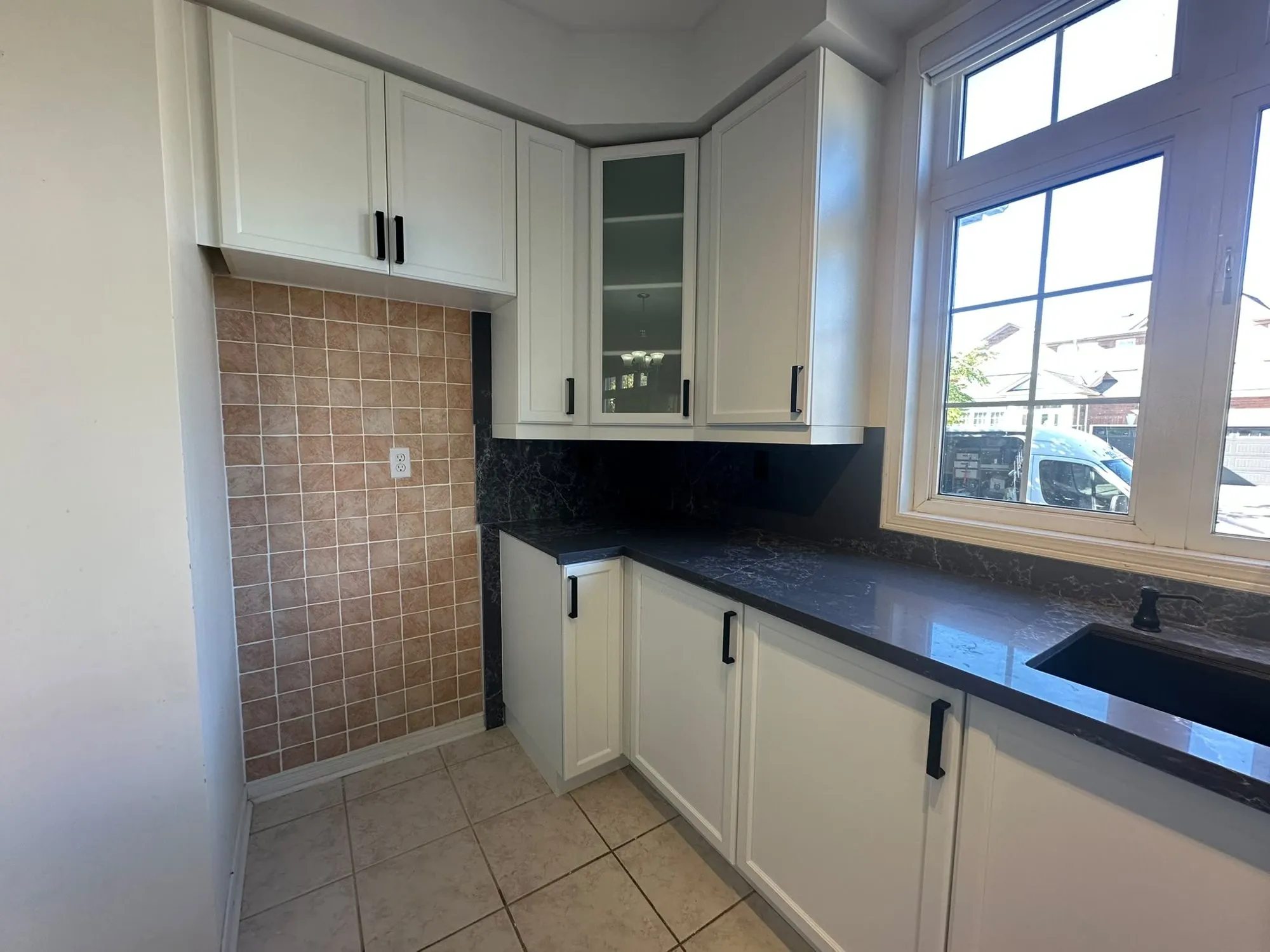 White shaker cabinets with black bar pulls above and below a dark stone countertop and matching dark backsplash
