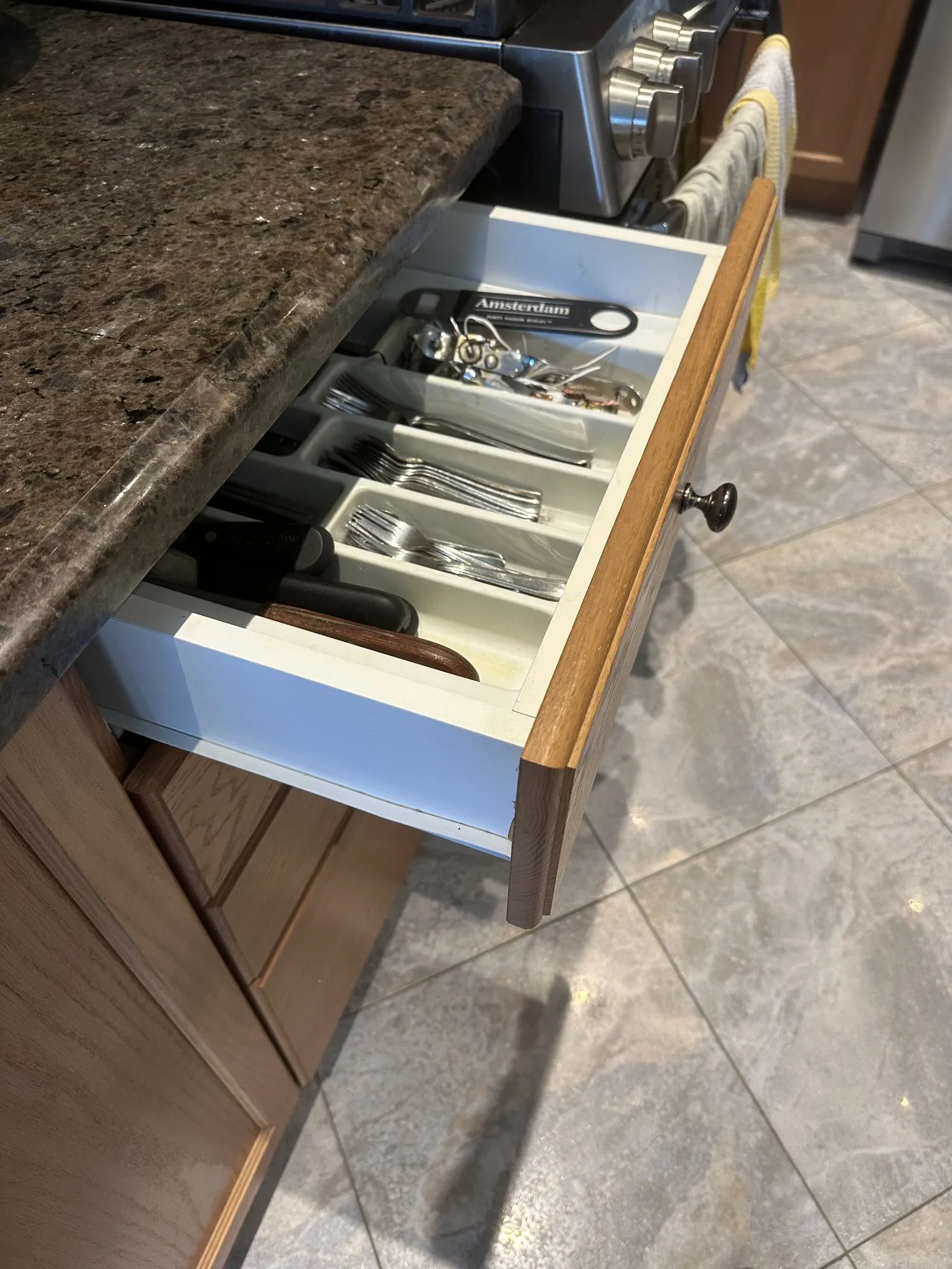 An original drawer pulled open before the work — a sound white melamine box behind a dated oak front with a small dark knob, on the old speckled granite