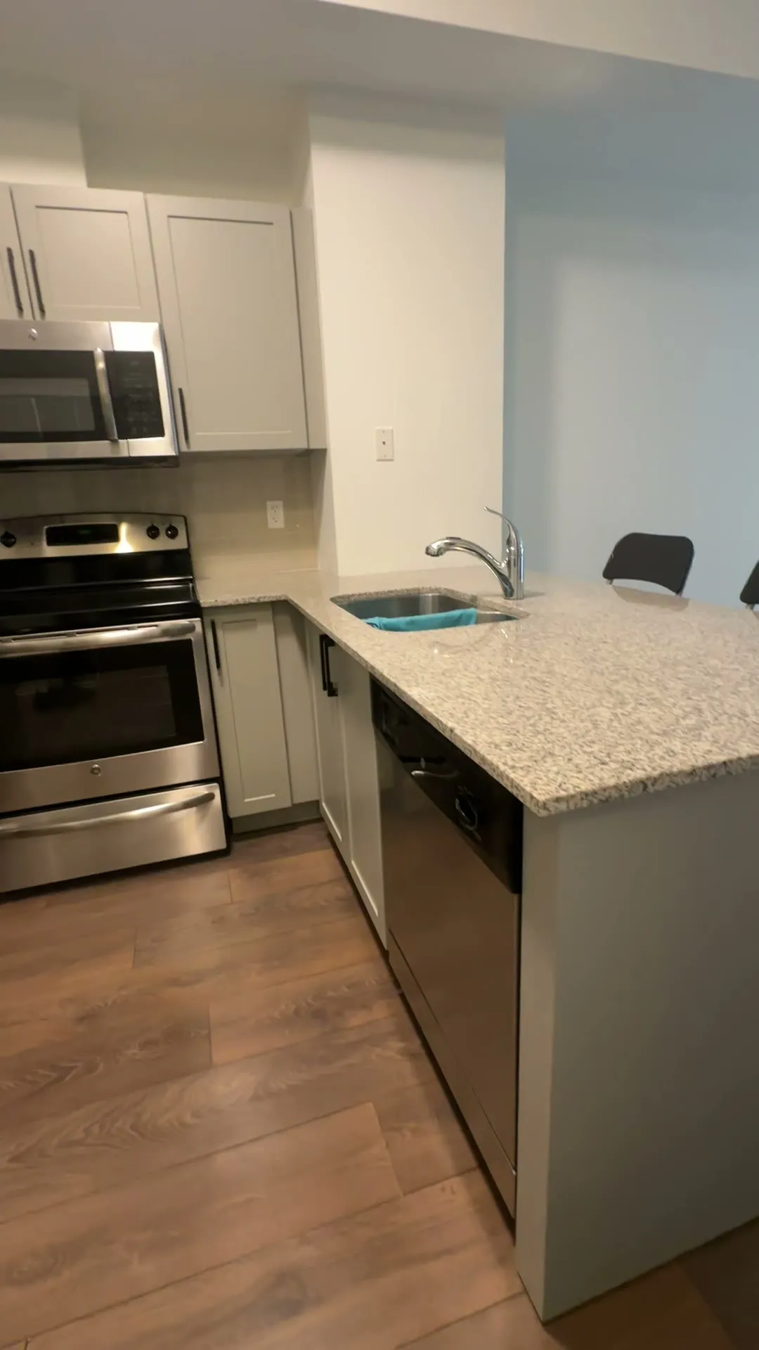 The finished Markham condo kitchen — Cashmere Grey shaker doors with black bar pulls, the original granite counter and tiled backsplash kept, looking across the peninsula to the range wall