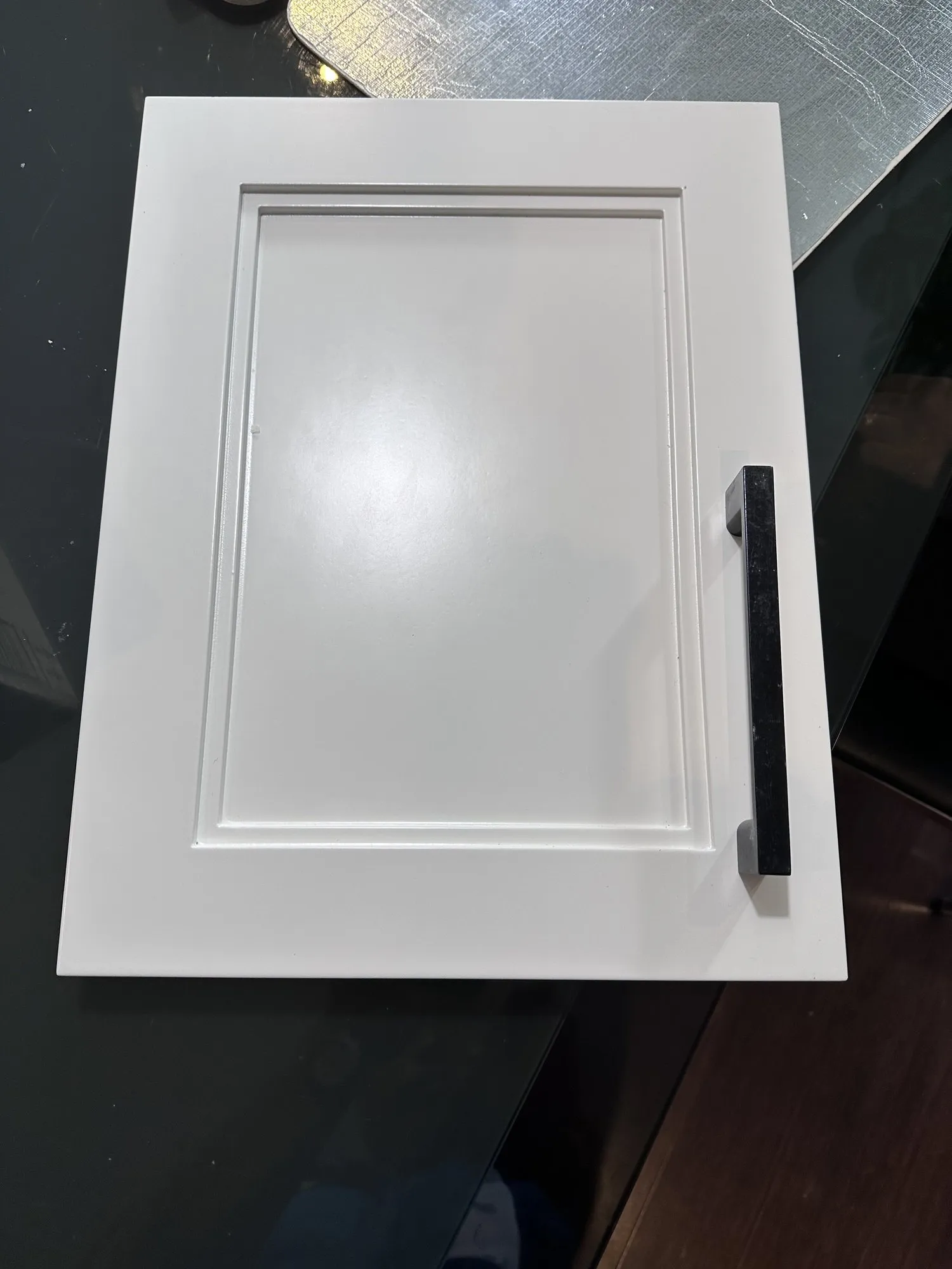 One finished white door with its new black handle fitted, photographed on the dark counter before installation