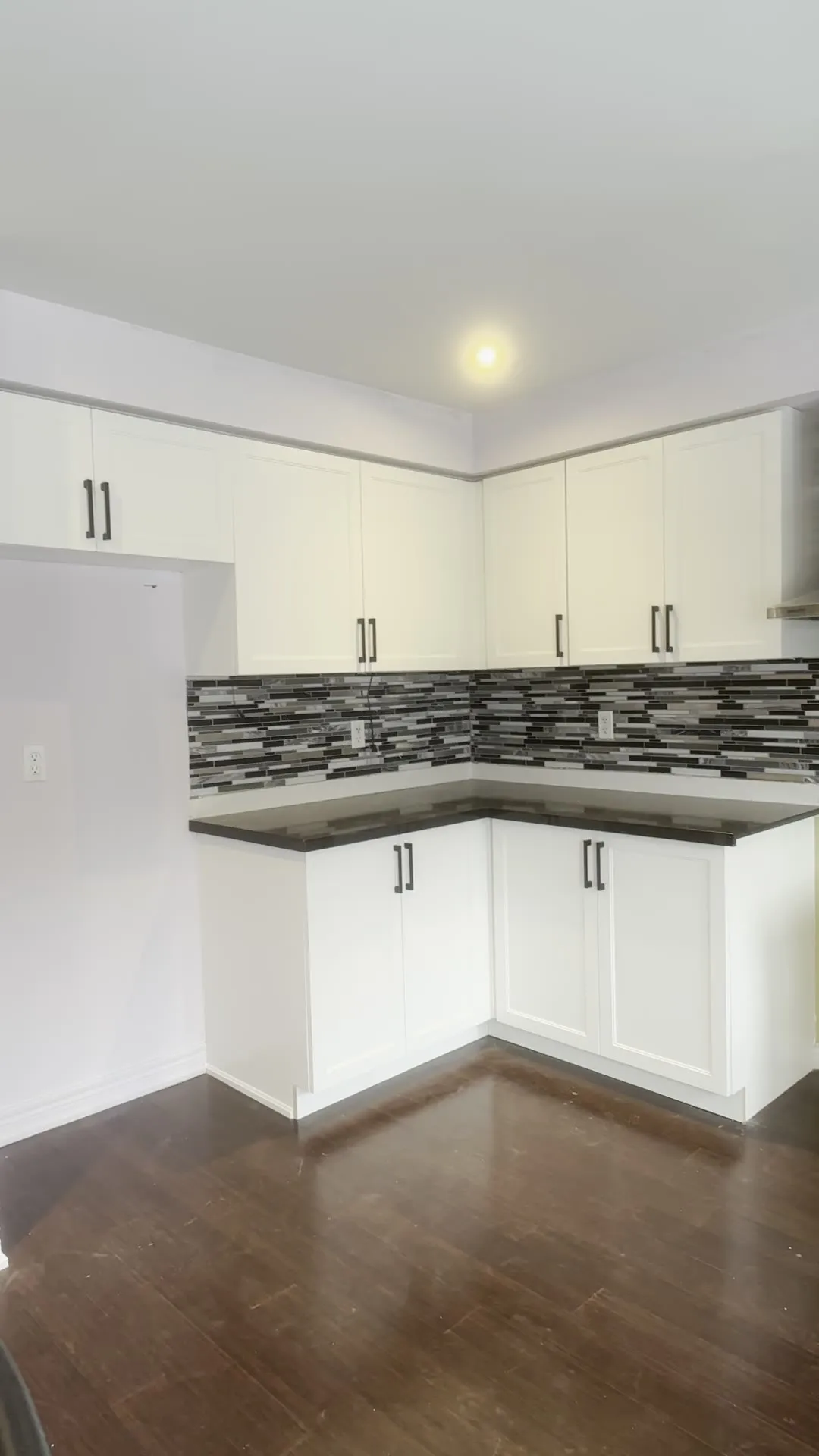 The finished Meadowvale Village kitchen — new white doors on the original boxes, with the dark counters, mosaic backsplash and hardwood floor unchanged