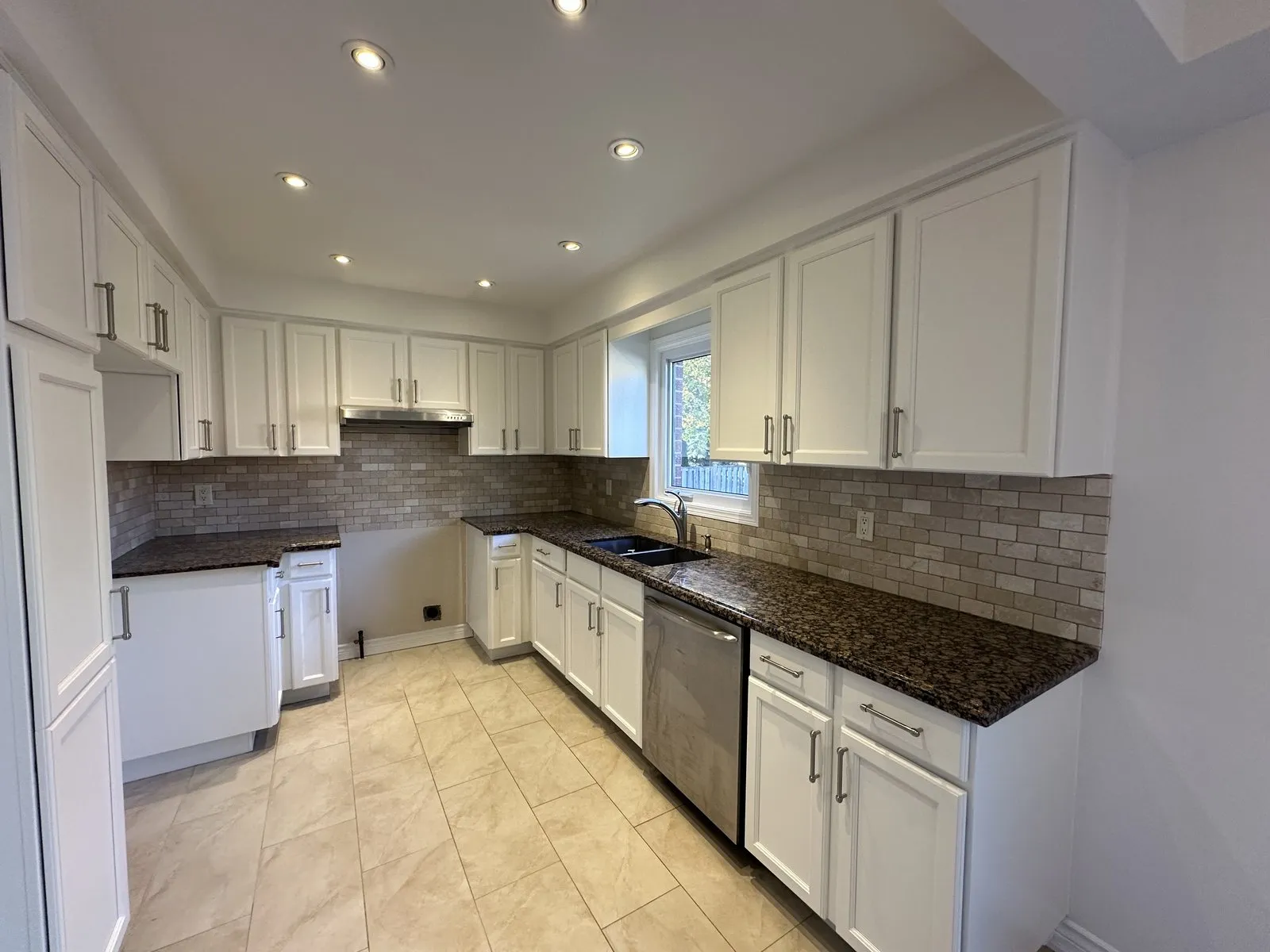 Long run of white Shaker base cabinets with brushed nickel pulls, a dishwasher and granite countertops