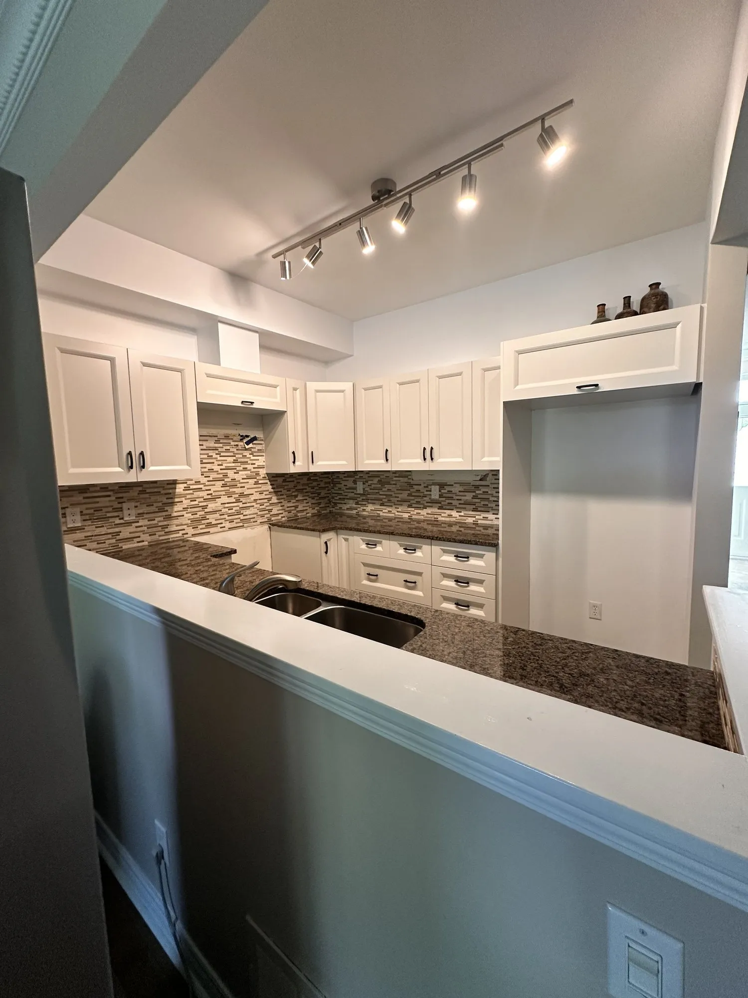 The finished kitchen with a new white cabinet box above the fridge return and a second one carrying the range hood, the mosaic backsplash and granite counter unchanged