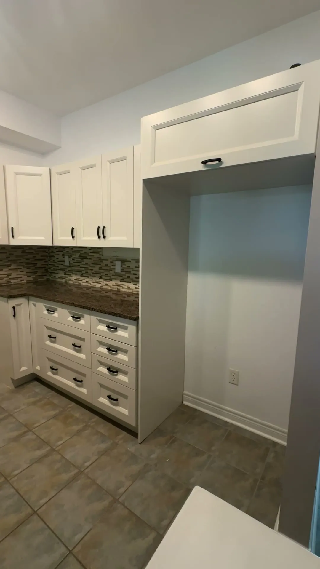 The finished Newmarket kitchen — white MDF doors on the original frames, the mosaic backsplash and granite kept, looking down the galley past the range to the fridge return