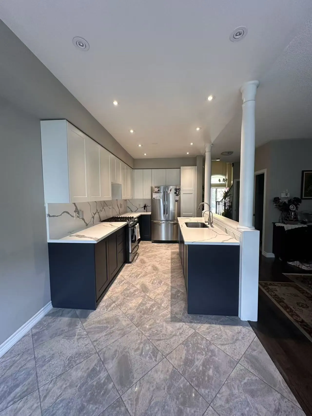 The same kitchen finished — white shaker uppers, charcoal bases, quartz counters, with the identical layout, floor and columns