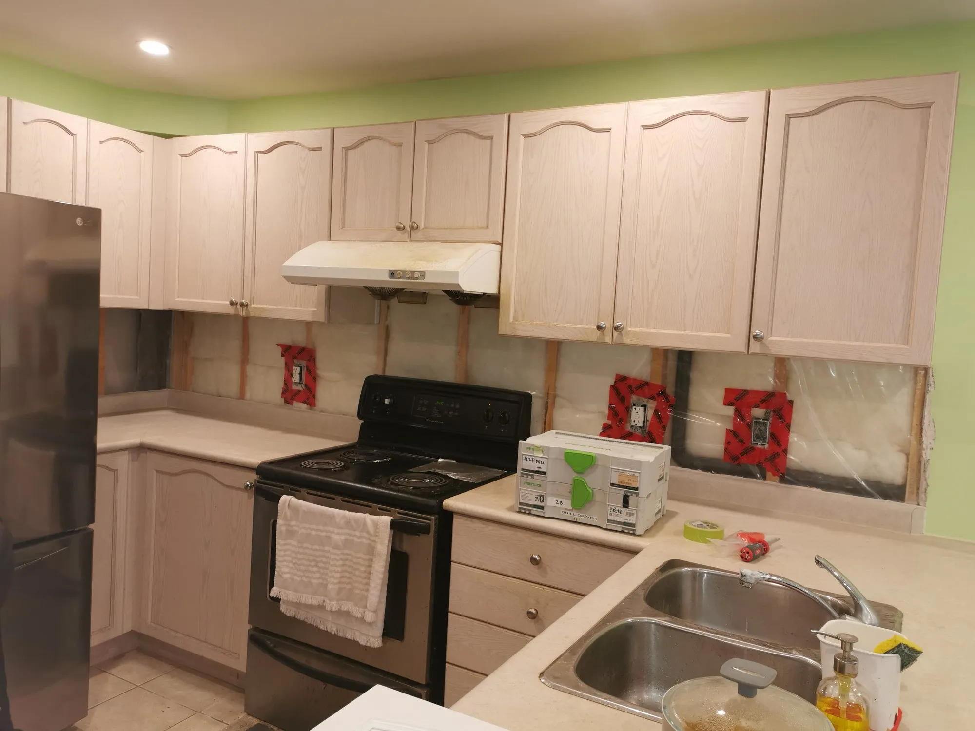 The original whitewashed oak kitchen with cathedral-arch doors and cream laminate counters, the backsplash already taken off and the outlets taped