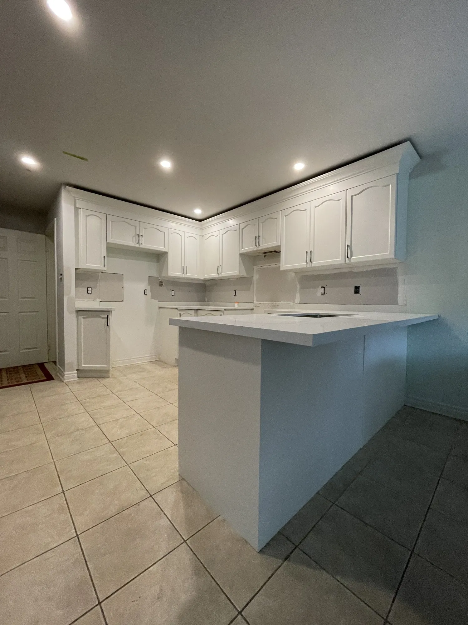 The finished kitchen with new white quartz counters on the peninsula, white refinished cabinets and crown moulding running the full ceiling line