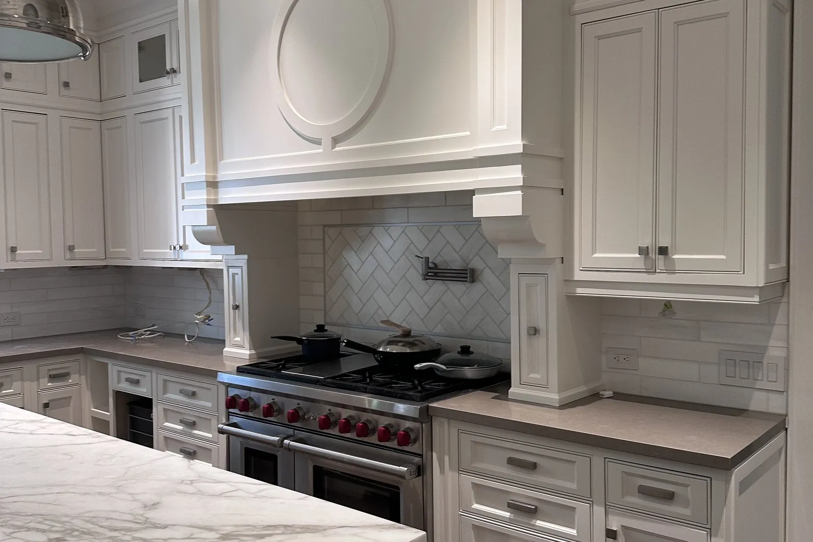 A herringbone tiled splashback behind a range, running up to a custom hood surround