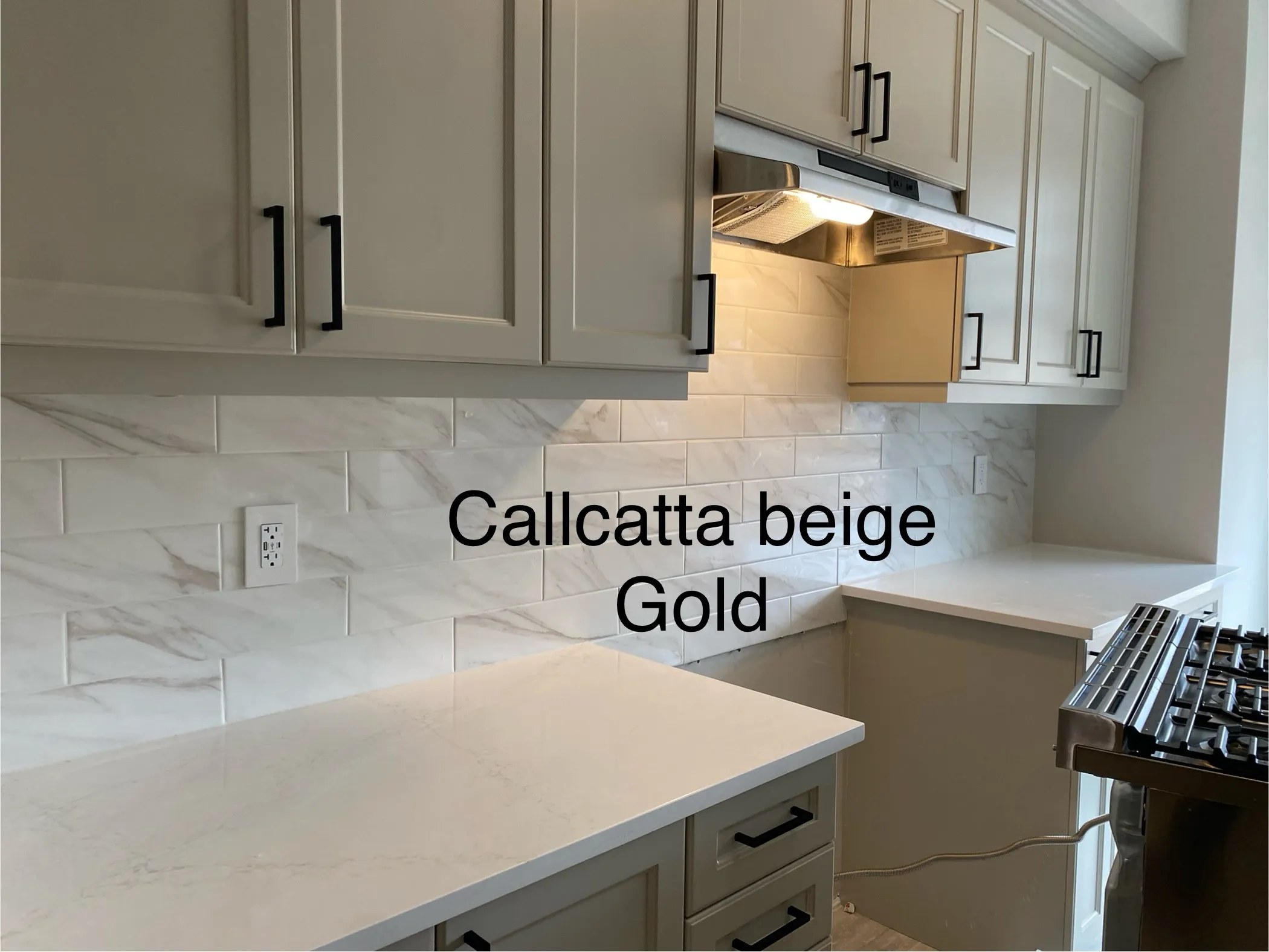 A finished Calacatta-look marble subway tile backsplash run full-height behind a range hood, quartz counters below