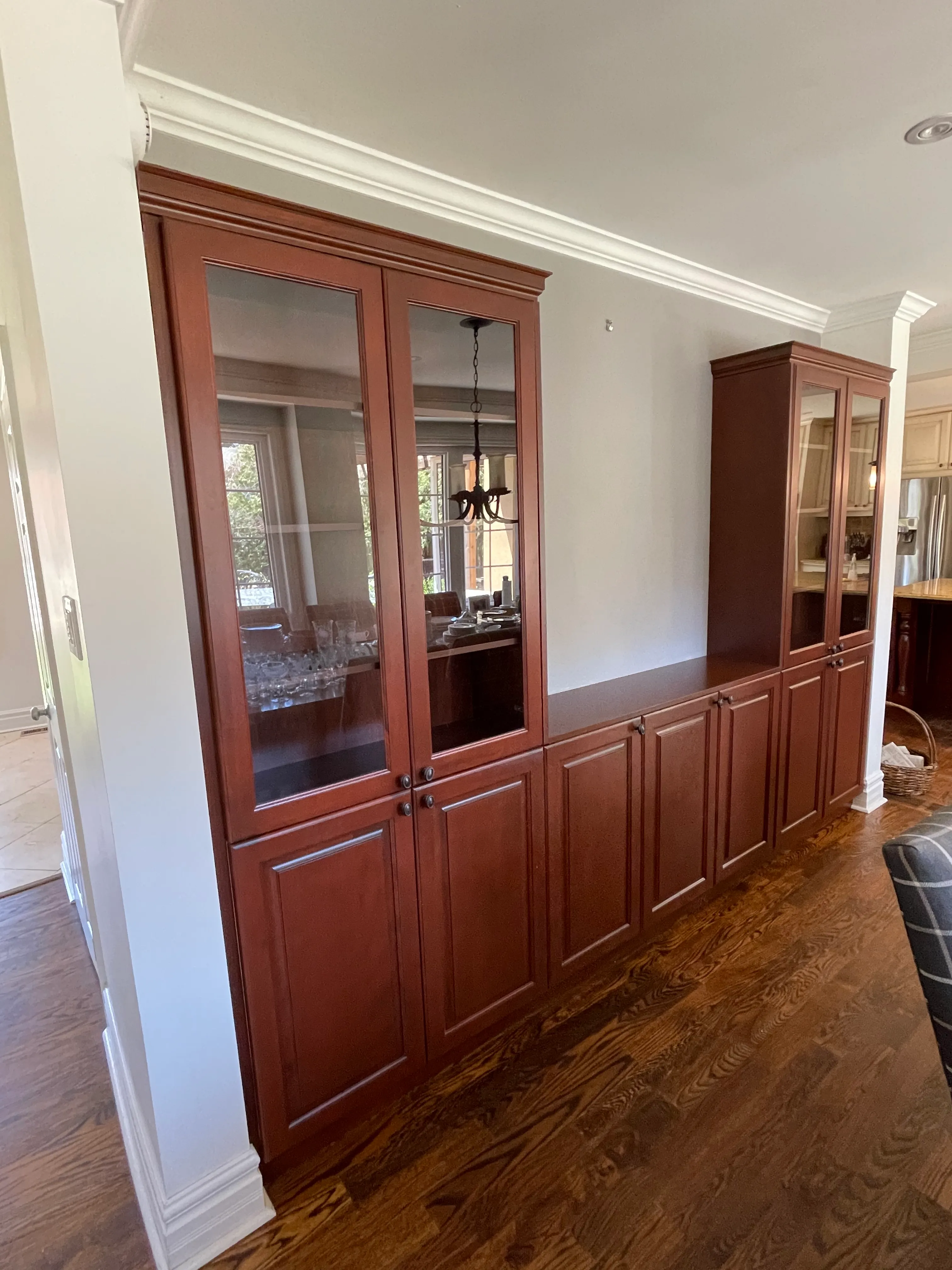 A built-in cabinet wall stripped and refinished in a rich cherry stain, glass-front doors and crown moulding, the grain reading through the finish