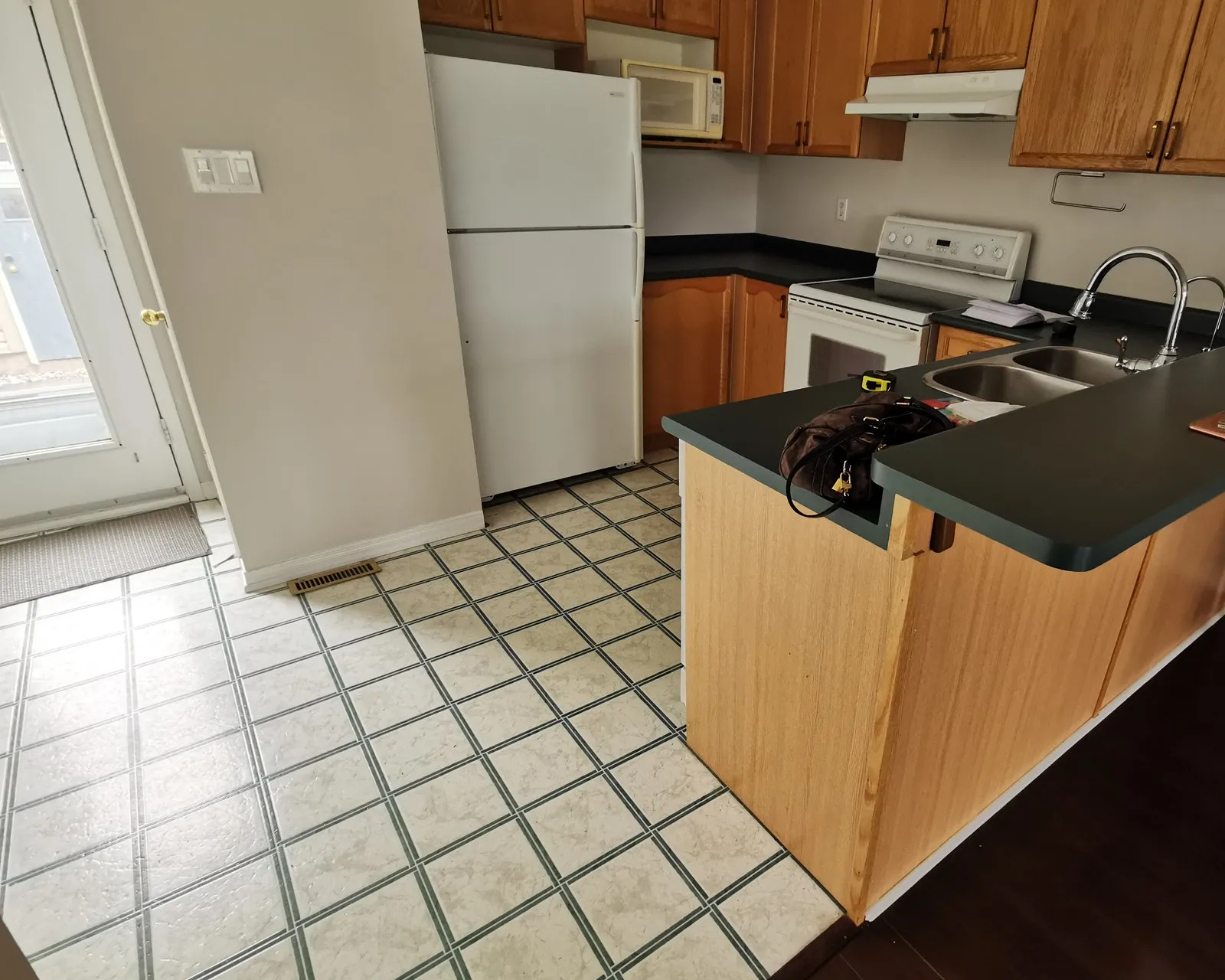 Before — A kitchen before and after — dark laminate tops on oak cabinets replaced with white quartz, on cabinets refinished in grey at the same time